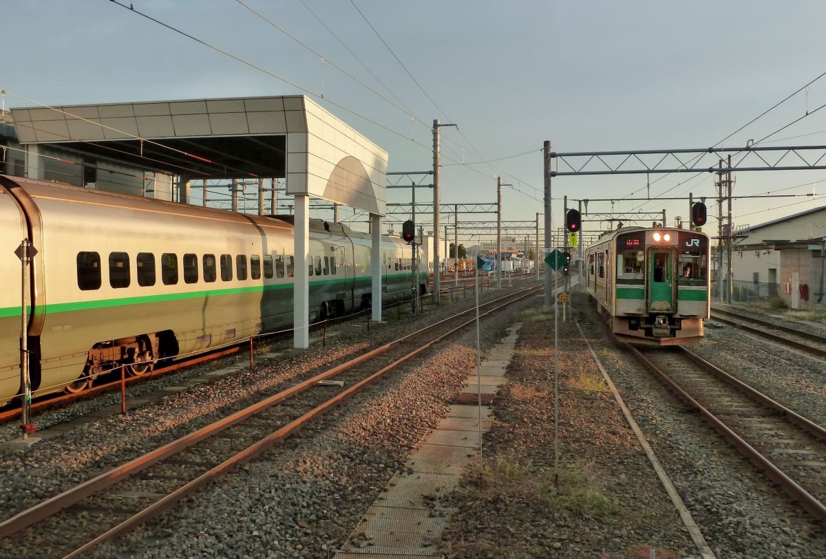 Serie 701 - die 5 Einsatzbezirke: Die Normalspur-Regionallinie von Fukushima aus zur Stadt Yamagata (auf einem Hochplateau im Gebirge) und weiter ins Hinterland bis Shinjô (ca 149 km). Hierfür wurden 9 Züge der Serie 701-5500 gebaut (1999). Die Linie wurde auf Normalspur umgespurt, damit die Shinkansen-Hochgeschwindigkeitszüge diese Gegend direkt von Tokyo aus erreichen können. So dauert die ca. 421 km lange Fahrt von Tokyo via Fukushima und Yamagata nach Shinjô heute rund 3 1/2 Stunden; im Fahrplan von 1973 brauchten die 1067mm-Spur Superschnellzüge noch rund 5 Stunden, die damaligen Schlafwagenzüge noch länger. Bild: rechts - Einfahrt des Zuges 701-5503 in Shinjô; links davon liegt ein 1067mm-Spur-Gleis einer Nebenlinie, und ganz links steht ein Shinkansen-Hochgeschwindigkeitszug in der Wartungshalle von Shinjô. 19.Oktober 2011.    