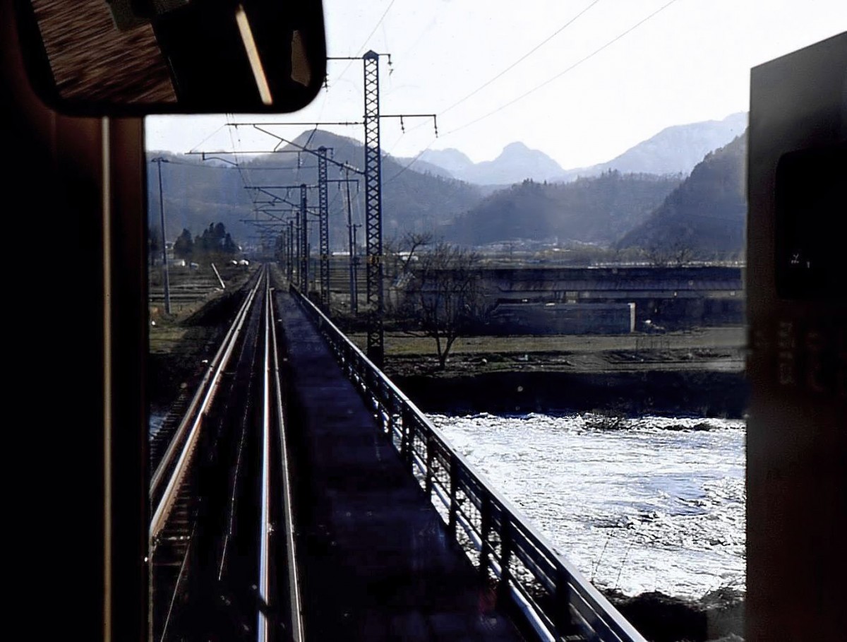 Serie 701 des Bezirks Akita - auf der alten Haupttransversale Tokyo-Yamagata-Akita: Um von Akita nach Yamagata zu gelangen müssen die hohen Berge im Hintergrund durchquert werden. Die rauschenden Bergbäche erfreuen den Betrachter, solange sie nicht zu äusserst bedrohlichen Sturzfluten heranschwellen. Bild bei Yokobori, aus Zug 701-33. 22.April 2003. 