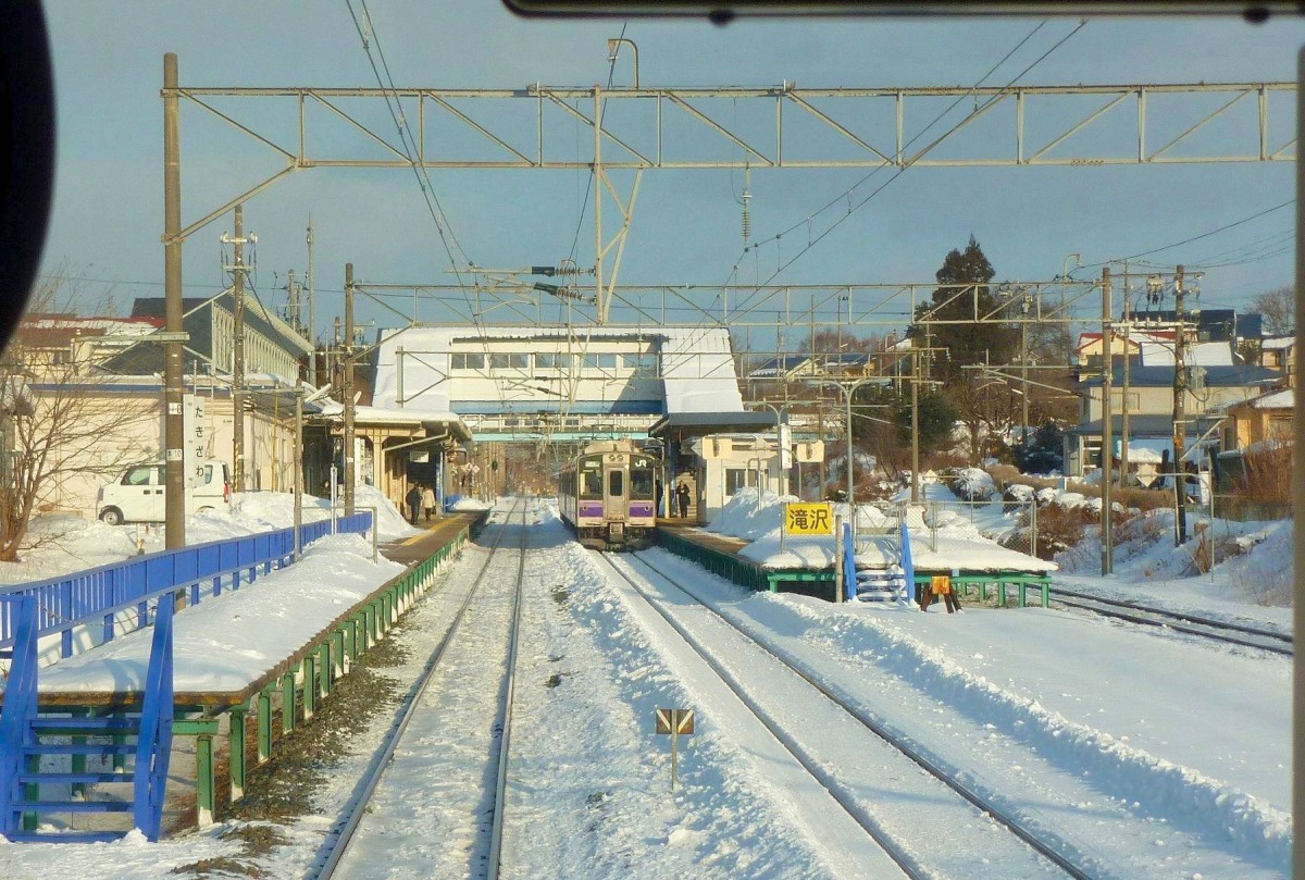 Serie 701 des Bezirks Morioka: Die Station Takizawa leuchtet in den Strahlen der Morgensonne; am Bahnsteig steht Zug 701-1008. 12.Februar 2013. 