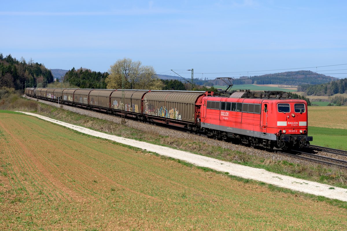 Sieht zwar aus wie ein Ganzzug, war aber die Übergabe nach Plattling, die am 15. April 2015 mit Zuglok 151 037 bei Darshofen fotografiert werden konnte. Zwischen den Bäumen erkennt man übrigens die Kirche von Krappenhofen.