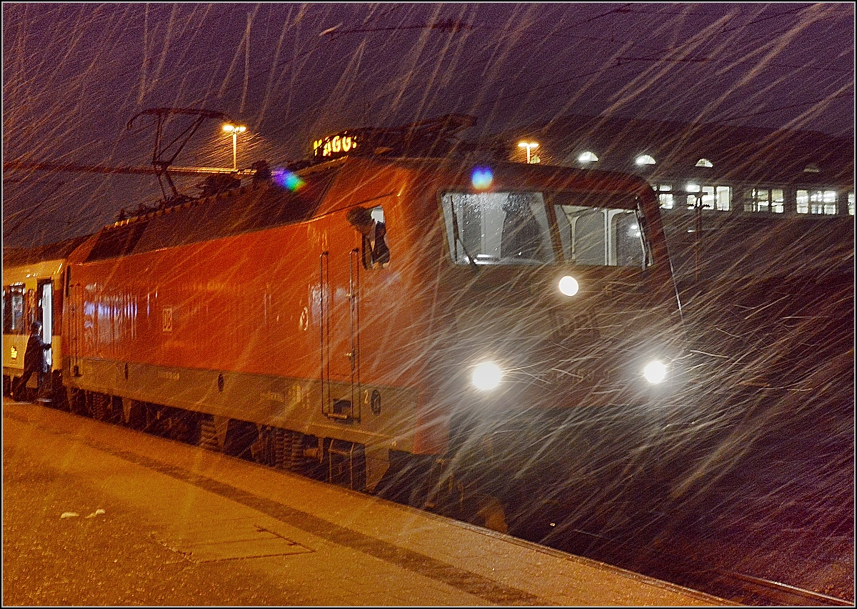 Singen am Abend. Die Zugbegleiterin schüttelt sich und steigt ein zur Abfahrt des Zuges. Der Wind schickt eine Schippe Schnee und eine Böe hinterher. Januar 2015.