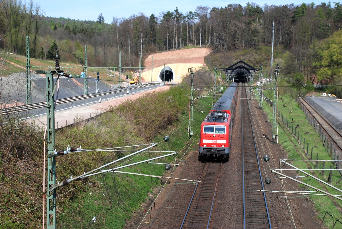 So sah es dann am 24.4.2010 aus : Die alte Strecke wird noch zweigleisig befahren, die neue Röhre, steht aber kurz vor Inbetriebnahme. Der neue Tunnel durfte nur befristet mit Sondergehmigung zweigleisig betrieben werden und ist heute wieder eingleisig (wie auch die sanierte alte Röhre), da Gleisabstand und Tunnelprofil nicht den Vorschriften für dauerhaften 2-gleisigen Betrieb entsprachen. 111 192 kommt mit RE aus Fulda. 