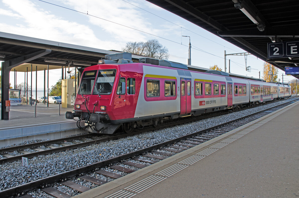 Sonntag den 26.11.2023 um 09:17 Uhr in Neuchâtel / Neuenburg (NE). Im Bahnhof Neuchâtel auf Gleis 1 in den Sektoren C + D fährt ein der NPZ DOMINO Zug mit der Zugnummer 7031 welcher von Buttes (ab 08:31 Uhr) über Môtiers NE – Travers - Auvernier – nach Neuchâtel (an 09:18 Uhr) verkehrt. Die Zugzielanzeige zeigt bei der Einfahrt in den Bahnhof nur oder bereits  Fermé“ an da er hier endet. Die Farbe am Zug ist weiss mit rosa bis dunkelrosa. Dieser ehemalige TRAVYS (Transports Vallée-de-Joux – Yverdon-les-Bains – Ste-Croix) Zug an welchem das “travys“ Logo entfernt ist und jetzt  SBB CFF FFS“ angeschrieben steht, da er an die SBB verkauft wurde, besteht aus folgendem Rollmaterial (Spitze – Schluss wie auf Foto):

ABt	 	NPZ DO  50 85 3943 985-3 CH-SBB  Steuerwagen mit 1. + 2. Klasse,

B	 	NPZ DO  50 85 2943 385-8 CH-SBB  Niederflurmittelwagen 2. Klasse,

RBDe	560 	DO  	     94 85 7560 385-7 CH-SBB  Triebwagen mit 2. Klasse und Gepäckabteil.                                 

Koordinaten GMS (Grad, Minuten, Sekunden): N 46° 59’ 48.3’’ O 6° 56’ 7.3’’