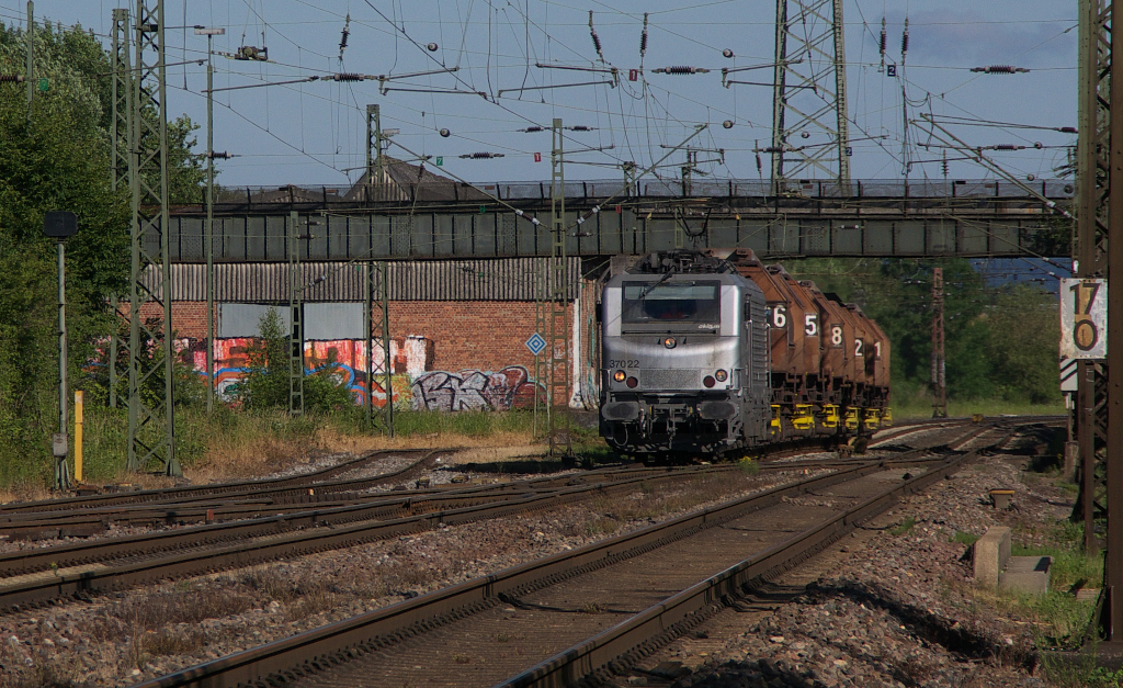 Sonntagmorgen - Das Wetter passte und so ging es nach Bous an die Strecke. In Höhe der alten Bahnmeisterei und des Stahlwerk Bous (früher Mannesmann Röhrenwerke) gibt es einen schönen Platz. Dieser ist etwas breiter, weil der Fahrdraht früher noch ein weiteres Gleis überspannen mußte und die Masten zurück gesetzt stehen. Bei Saarstahl wird rund um die Uhr gearbeitet, egal ob Sonn- oder Feiertag. Daher muß auch der Suppennachschub nach Völklingen rollen. Akiem 37022 ist mit vollen Torpedowagen von Dillingen / Hochofen nach Völklingen unterwegs. 15.06.2014 - Bahnstrecke 3230 Saarbrücken - Karthaus