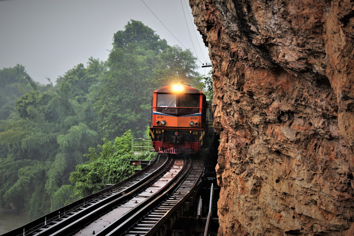 SRT ALS 4131 unterwegs unter strömendem Regen mit Ordinary (ORD) 258 von Nam Tok nach Thon Buri auf dem Tham-Krasae-Viadukt auf der  Death Railway  zwischen den Bahnhöfen Saphan Tham Krasae und Tham Krasae. Rechts eine bedrohliche Felswand, links der Fluss Kwai Noi und dazwischen die  Todesbrücke , die einen tragischen und geschichtlichen Hintergrund bei sich trägt, denn im 2. Weltkrieg wurde sie von Zwangsarbeitern und Kriegsgefangenen erbaut, deren unmenschliche Behandlung ein Kriegsverbrechen darstellt. Sonntag, 6. August 2017
