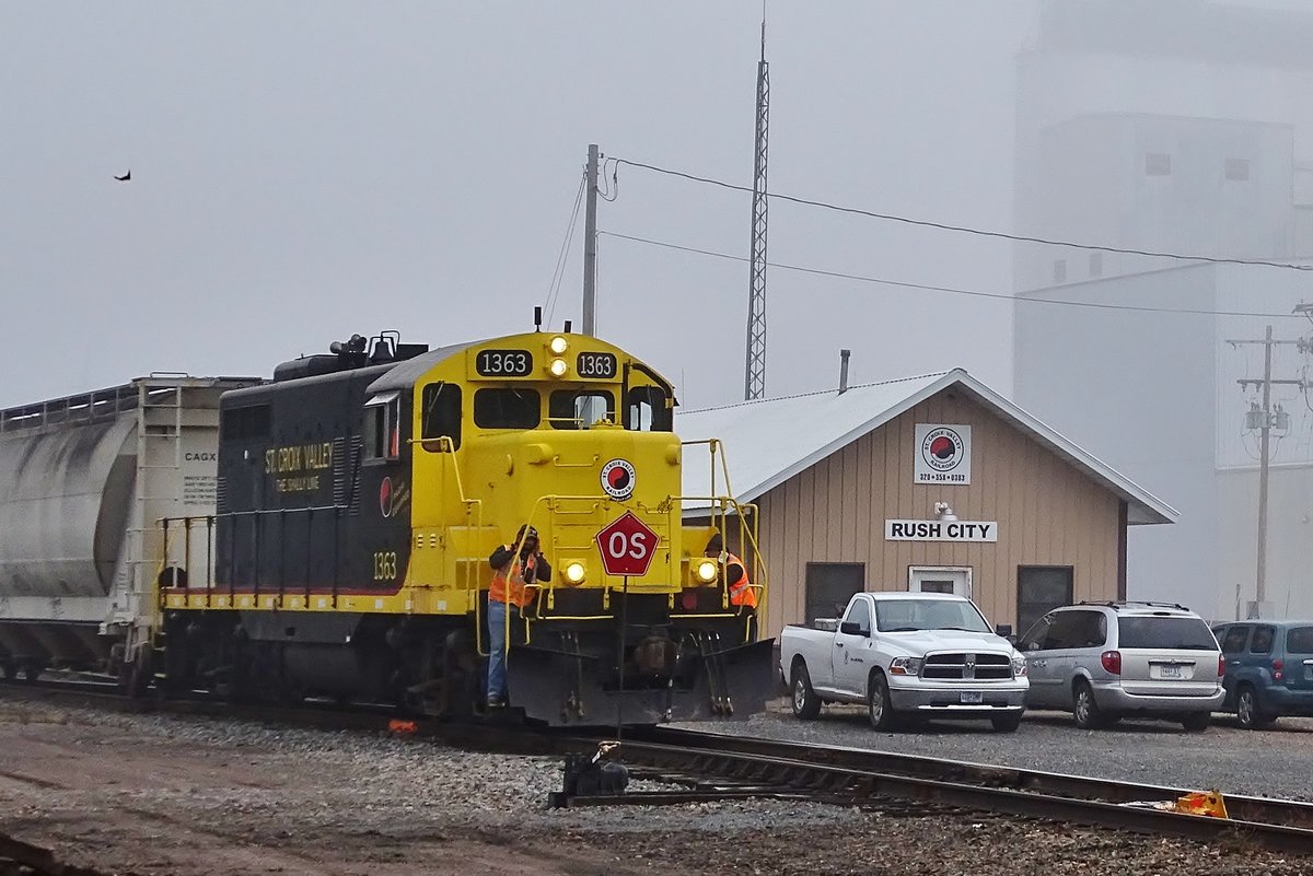 St Croix Valley Railroad 1363, EMD GP9,Baujahr 1954 beim Rangieren im Rush City Depot,die beiden Yardmen die vorne auf der Lok stehen halten sich die Ohren zu wegen dem extrem lauten Signalhorn das der Lokführer erdröhnen läßt weil er gleich einen Bahnübergang überfährt.
Aufgenommen in Rush City,Minnesota am 6.Okt. 2017
