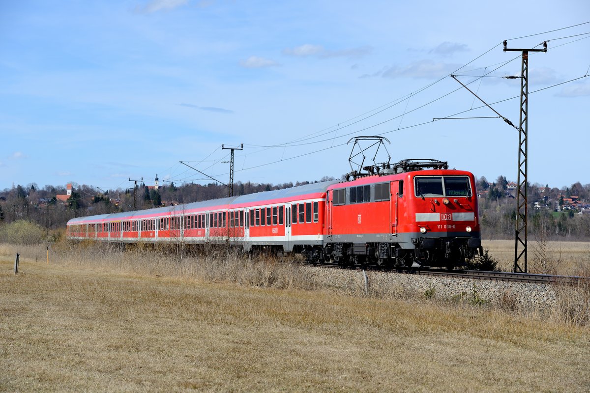 Standortwechsel ins Murnauer Moos. 111 036 ist mit der RB 59549 vor kurzem die Hechendorfer Rampe heruntergerollt und wird gleich die Kirche bei Weichs passieren. Im Hintergrund ist Murnau zu erkennen (14. April 2013).
