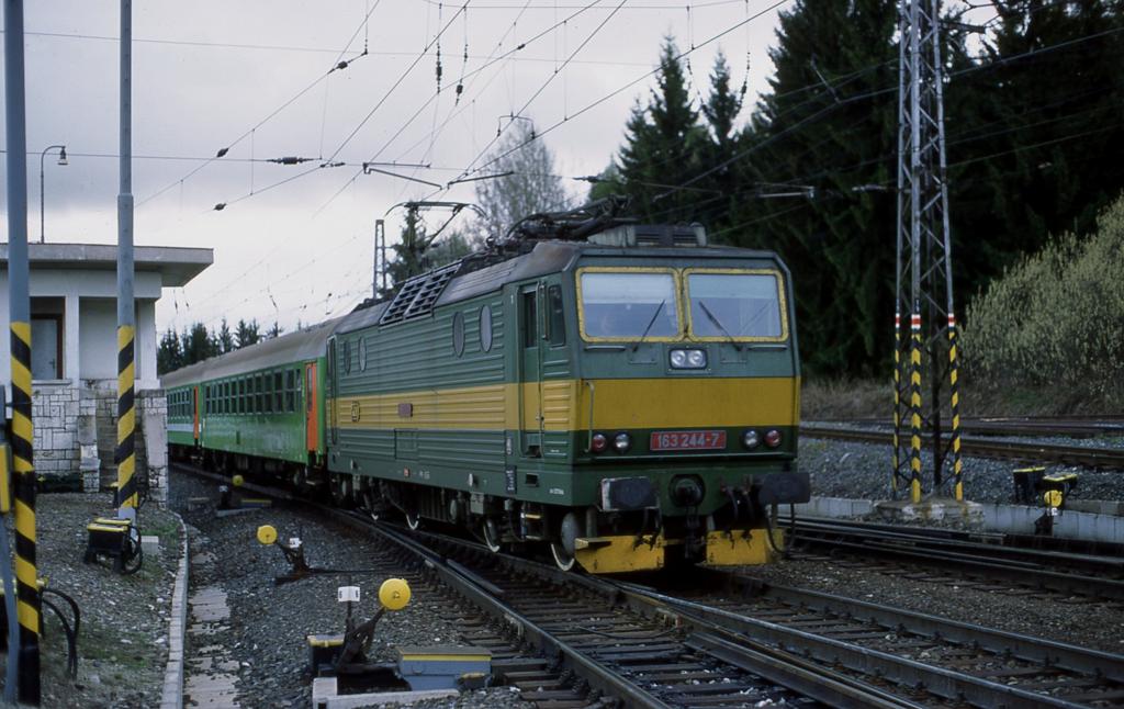 Strba am Fu� der Hohen Tatra ist ein sehr interessanter Bahnhof.
Im oberen Teil, innen im Bahnhof Geb�ude befindet sich die Talstation
der Zahnradbahn. Unten, quasi auf Ebene  Null  liegt der Bahnhof. Dieser
zieht sich in weitem Bogen durch zwei lang gestreckte Kurven. An den Zufahrten
und auch von der B�schung von oben herab kann man den Bahnhof wunderbar einsehen
und hat viele M�glichkeiten, sich einen Fotopunkt zu suchen. Am 3.5.2003 versuchte ich es in der �stlichen Zufahrt und fotografiere dort die slowakische 163244 mit ihrem Os aus Poprad bei der Einfahrt.