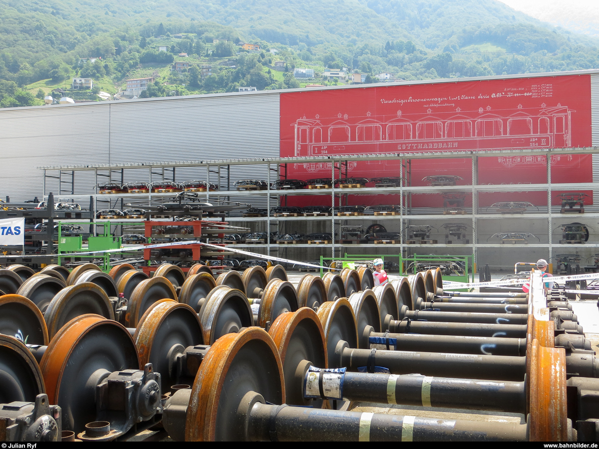 Tag der offenen Tür im SBB Industriewerk (ehemals Hauptwerkstätte) Bellinzona am 15. Juni 2013. Vor der Halle lagern Dutzende von Achsen und in einem überdimensionalen Regal finden sich Stromabnehmer aller Art. An der Wand hängt eine Seitenansicht eines vierachsigen Personenwagens der Gotthardbahn.