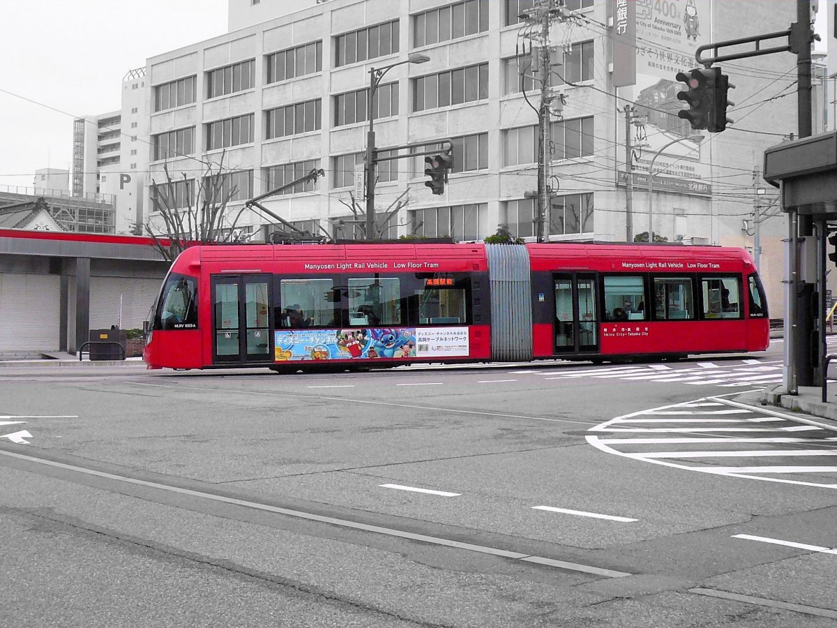 Takaoka Manyô-Linie, neue Wagen Serie 1000: 6 solche Wagen vom Typ LRV (Light Rail Vehicle) kamen zwischen 2004 und 2009 in Betrieb; gleichartige Wagen stehen auch in der benachbarten Stadt Toyama im Einsatz. So etwas ist in Japan in den Regionen finanziell nicht möglich, doch mit Blick auf einen wirklichen Publikumserfolg wäre eine sofortige Umstellung aller Grundkurse auf neue Wagen besser gewesen. Aufnahme des Wagens 1003 in der Innenstadt von Takaoka, 28.Februar 2010.  