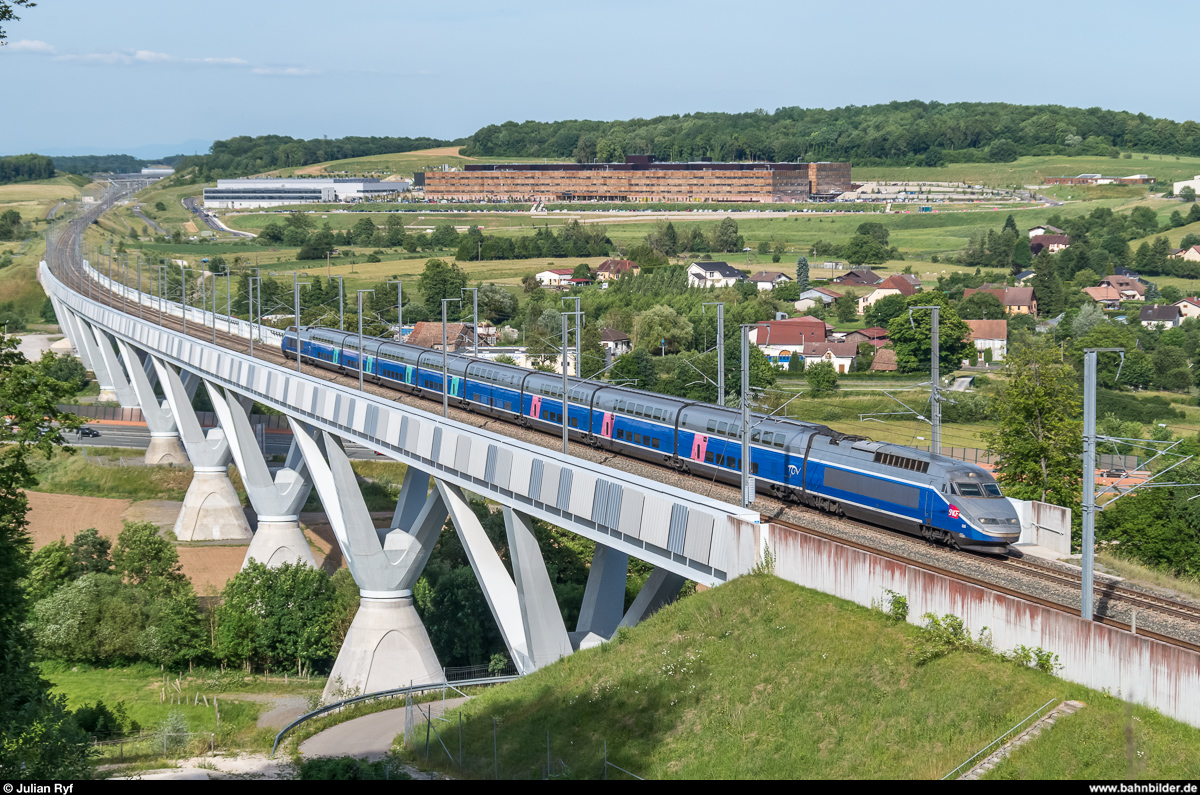 TGV Réseau-Duplex 606 hat am 16. Juni 2017 als TGV 6710 aus Mulhouse Ville gerade den Bahnhof Belfort-Montbéliard TGV (ganz hinten links) verlassen und strebt nun Besançon Franche-Comté TGV, Dijon Ville und Paris Gare de Lyon entgegen. Der Zug verlässt hier gerade den Viaduc de la Savoureuse auf der LGV Rhin-Rhône. Beim grossen Gebäude im Hintergrund handelt es sich um das Hôpital Nord Franche-Comté.
