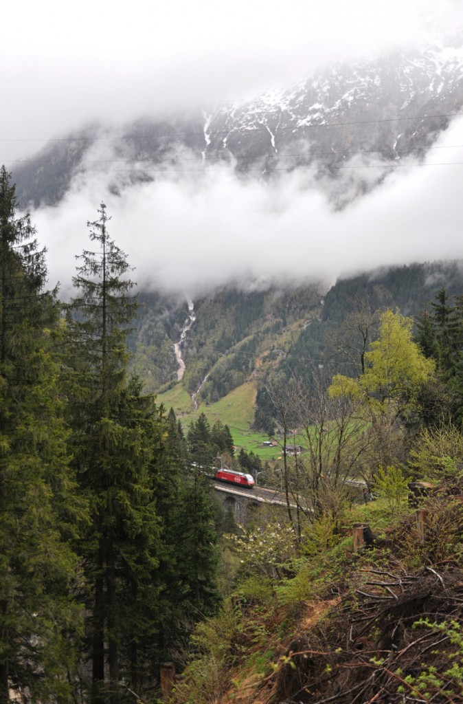 Tief hängende Wolkenbänder zeugen vom turbulenten Wetter, welches am 28.04.2015 im Urner Reusstal vorherrschte. Während die frisch verschneiten Bergspitzen noch in den Wolken verschwinden, fährt eine Re 460 mit ihrem Interregio bei Nieselregen über die Mittlere Meienreussbrücke. 