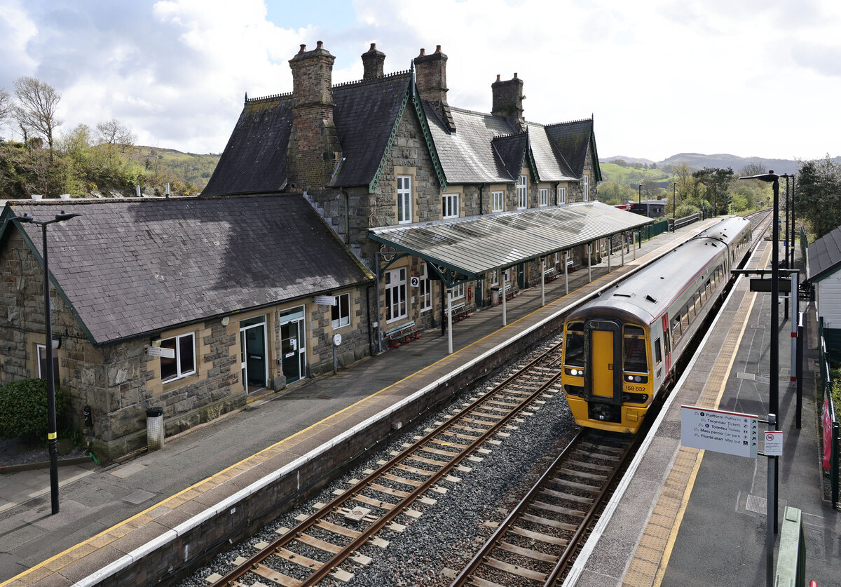 Transport for Wales / Trafnidiaeth Cymru: Das imposante Bahnhofsgeb�ude von Machynlleth. Triebzug 158 832, der von Pwllheli her gekommen ist (Cambrian Coast Line), wartet auf das Eintreffen des Zuges von Aberystwyth her (Cambrian Main Line), der hinten ankuppeln wird. 18.April 2026  