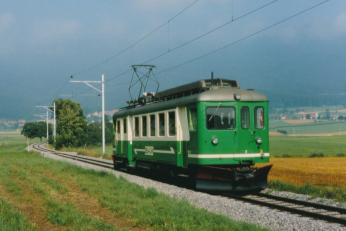 Transports de la région Morges-Bière-Cossonay, MBC/BAM.
ERINNERUNG AN DIE TRIEBWAGEN ABDe 4/4 MIT DEN BETRIEBSNUMMERN 1-5.
Die Dampflokomotiven wurden im Jahre 1943 durch die Inbetriebnahme der SWS SAAS ABDe 4/4 1-4 mit der unsymmetrischen Stirnfront verdrängt.
Noch bis in das Jahr 1994 war hauptsächlich die Zweiglinie Apples-L’Isle das Tätigkeitsgebiet der BDe 4/4, da die neuen stärkeren Be 4/4 11,12, 14 und 15 für die Bewältigung des Güterverkehrs sowie die Führung der Personenzüge auf der Hauptstrecke Morges-Bière eingesetzt wurden.
Durch die Anschaffung der neuen Güterlokomotiven Ge 4/4 21-22 im Jahre 1994 wurden die BDe 4/4 1, 3 und 4 endgültig aus dem Personenverkehr zurückgezogen und verschrottet.
Noch während den Probefahrten der Ge 4/4 21 im August 1994 wurde der BDe 4/4 2 mit neuem Anstrich anlässlich einer seiner letzten Fahrten als Reisezug bei Pampigny-Sévery verewigt.
Foto: Walter Ruetsch 
    