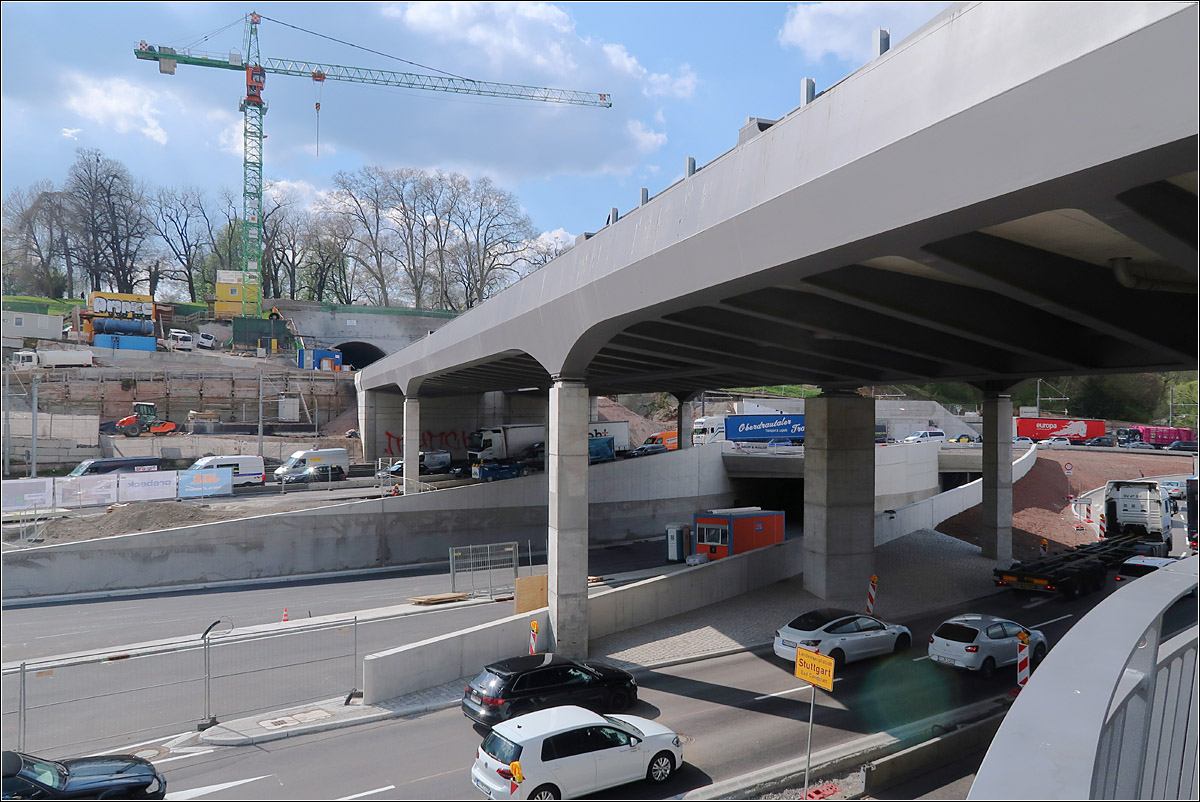 Treffen zweier Großbaustellen -

Zwischen Neckar und Rosensteinbark treffen die beiden derzeit größten Verkehrsbauprojekte Stuttgarts aufeinander. Oben die neue Neckarbrücke mit dem Portal des Rosensteintunnels für den Fern- und Regionalverkehr. Das zweite Portal für den S-Bahntunnel unter dem Rosensteinpark ist im Bild von der Brücke verdeckt. 
Unter der Brücke sind die schon weitgehend fertiggestellten Tunnelrampen des zweiten großen Projektes zu sehen. Ein langer vierspuriger Stra0entunnel unter dem Rosensteinpark für die Bundesstraße 10.
Hinten unterquert zudem die Stadtbahnlinie U14 die neue Bahnbrücke. Diese ist im Bild an den Oberleitungsmasten erkennbar.

Der Fußgängersteg wird später auch noch die B10 auf der Südseite der Bahnbrücke überqueren, hier im Bild auf der linken Seite. Fertiggestellt ist aber schon die Rampe hinunter zu den Schiffsanlegestellen.

Stuttgart-Bad