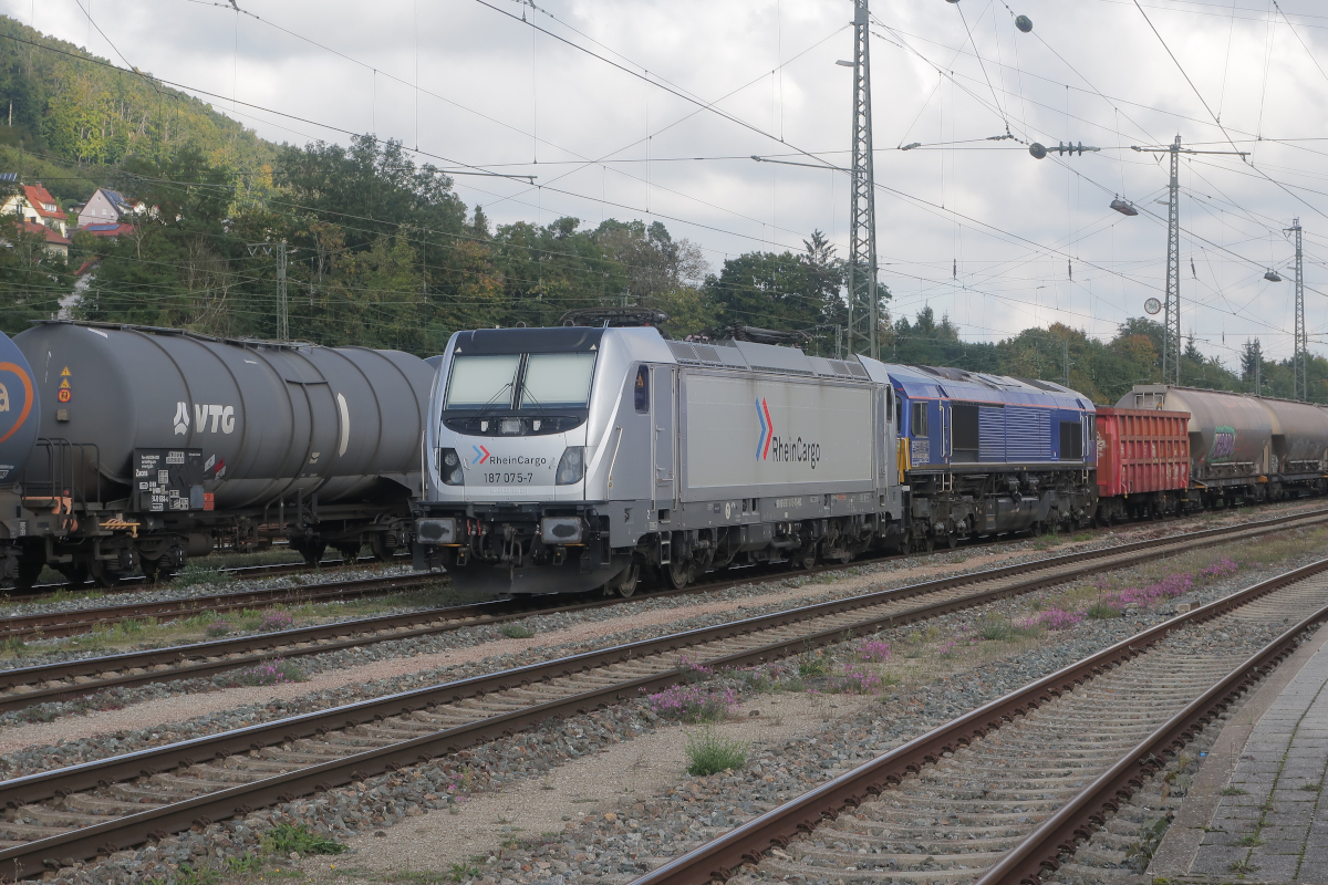Treuchtlingen am 1. Oktober 2025: Auf Gleis 9 legen die 187 075 D-RHC der Rheincargo und die  Class 66  1266 022-3 D-BRLL eine längere Pause ein. Am Haken haben die beiden Lok einen Zug mit mindestens 17 Waggons des Typs Uacs, beladen mit Braunkohlestaub.
Wegen ihrer lang gestreckten Bauweise, dem hohen Rahmen und den niedrigen Aufbauten erschien mir die Class 66 immer niedriger als andere Lokomotiven. Doch aneinander gekuppelt erweist sich die Class 66 über Dach etwa so hoch wie die 187 über Dach.
1.10.2025