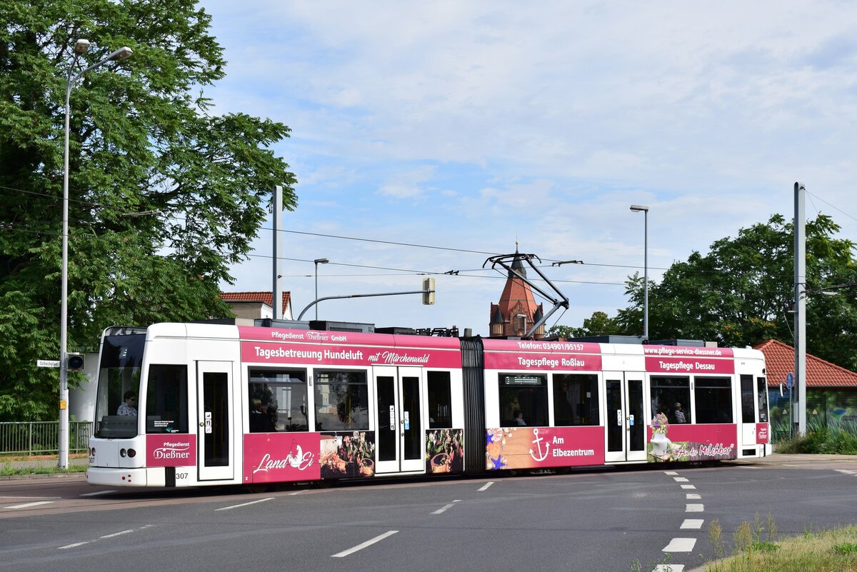 Triebwagen 307 fällt mit seiner fast schon pinken Werbung sehr auf. Der Triebwagen trägt Werbung für einen Pflegedienst. Hier überquert der Triebwagen gerade den Auenweg mit dem Kirchturm der Philipp Melanchton Kirche im Hintergrund. 

Dessau 28.07.2020