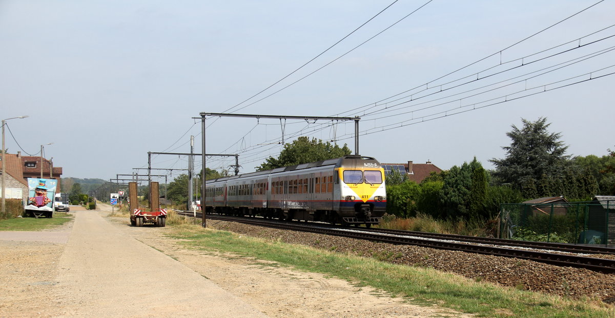 Triebzug 411 von der SNCB fährt als R 5363 von Hasselt(B) nach Maastricht(NL)  und kommt aus Richtung Hasselt(B) und fährt in Richtung Tongeren(B) und hält gleich in Tongeren(B) und fährt dann weiter in Richtung  Liège(B).
Aufgenommen an einem Weg in s'Herenelderen(B).
Bei Sommerwetter am Nachmittag vom 16.8.2018.