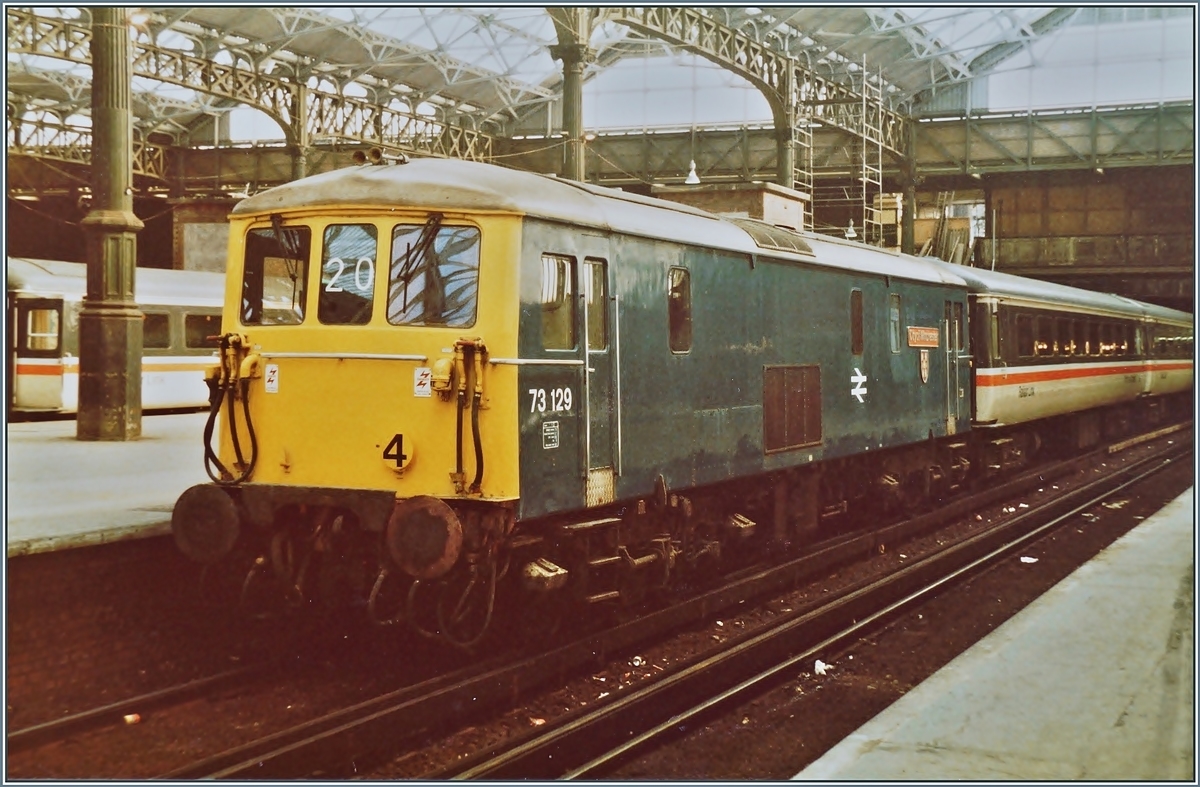 Trotz fehlenden Pantographen ist dies nicht (nur) eine Diesel- sondern eine E-Lok. Die Class 73 bezieht ihre Energie aus einer Stromschiene. 
Hier die 73 129 der Britisch Rail mit dem Gatwick-Express in London Viktoria am 18. Juni 1984. 
(Fotograviertes Fotos)
