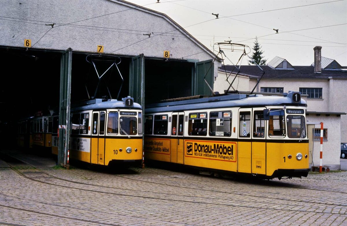 TW 10 und TW 1 der Baureihe GRW 4 warten vor dem früheren Depot in der Nähe der Station Westplatz auf ihre Nutzung auf der Linie 1 der Ulmer Straßenbahn.
Datum: 29.09.1984
