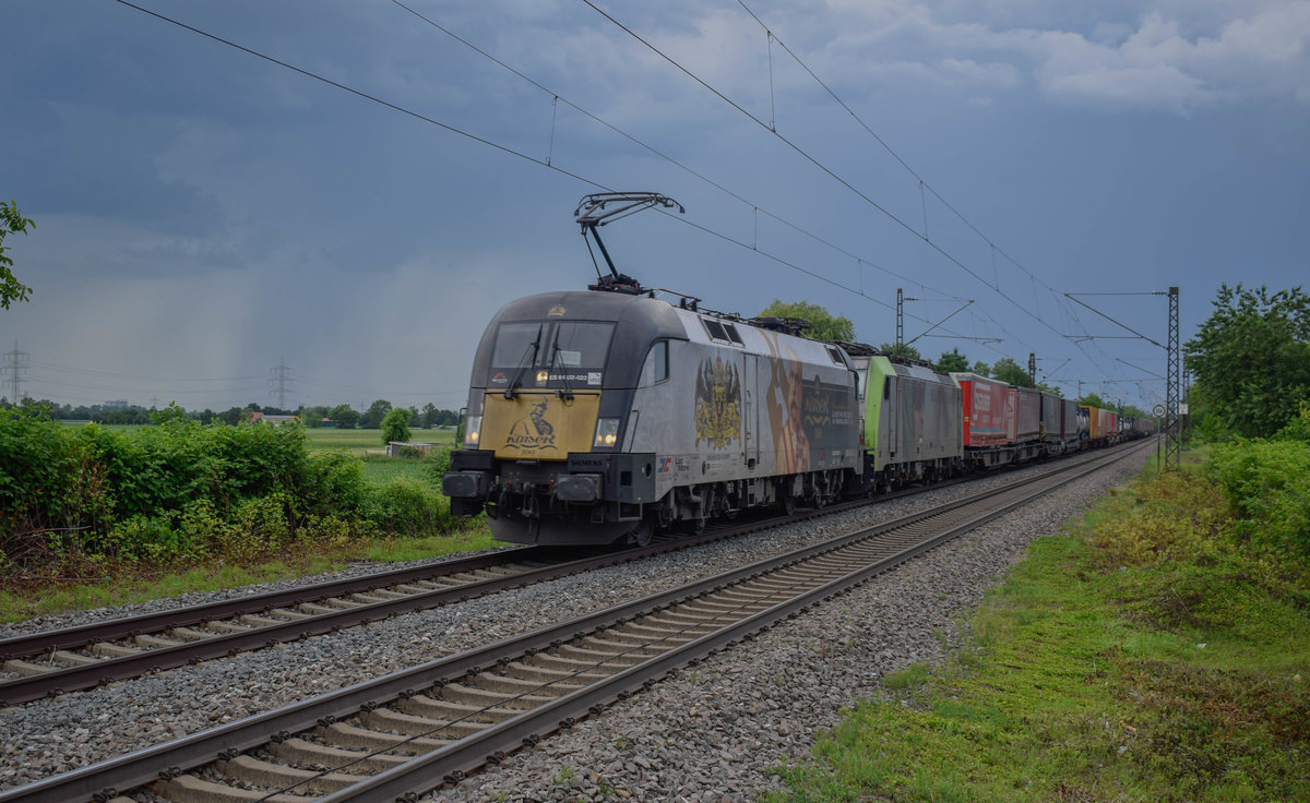 TXL 182 523 entflieht mit einer kalten BLS 486 und dem 42013, Wanne-Eickel Wst - Gallarate der Regenfront im Hintergrund. Aufgenommen am 30.05.2018 am Bahnsteigende des Haltepunkts Buggingen.