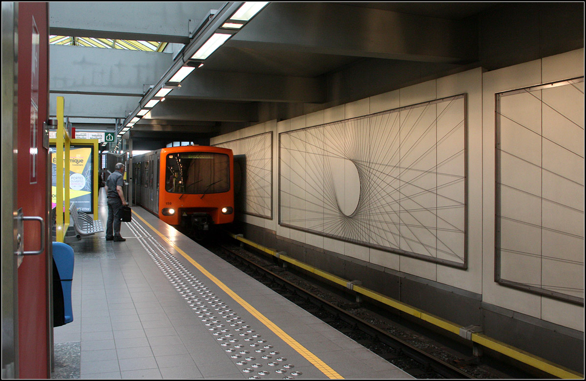 U-Bahn im Linksverkehr -

Die noch oberirdische Station Delacroix am Kanal Charleroi-Brüssel in Anderlecht (Brüssel).

Der nordwestliche Streckenast der Brüssler U-Bahnlinie 2 wird im Linksverkehr befahren. Durch die übereinander liegenden Bahnsteige an der Station Gare du Midi erfolgt die Eigenkreuzung niveaufrei. Ursprünglich war ab Beekant die Strecke eine Zweigstrecke der Linie 1. In der viergleisigen Station Beekant mussten die U-Bahnzüge Kopf machen. Dadurch ergab sich dann der Linksverkehr in Richtung Heysel. 2009 wurde dann dieser Streckenast zum Teil der Linie 2 und der Linksverkehr wurde beibehalten und so kann auch heute in Beekant am gleichen Bahnsteig gegenüber umgestiegen werden, wenn man mit der Linie 1 aus der Innenstadt kommt und auf diesem Abschnitt weiter fahren will.

Übrigens trifft die Linie 2 auf ihrem Weg in Richtung Heysel an der Station Simonis auf den anderen Endpunkt der Linie 2. Von der im Bild zu sehenden Bahnsteigseite der Station Delacroix bis Simonis sind es vier Stationen, auf der anderen Seite sind es 13 Haltestellen. Wir wählten den langen Weg um die Innenstadt von Brüssel herum und konnten so die Zeit eines Gewitters überbrücken, das gerade über Brüssel hereingebrochen war.

23.06.2016 (M)