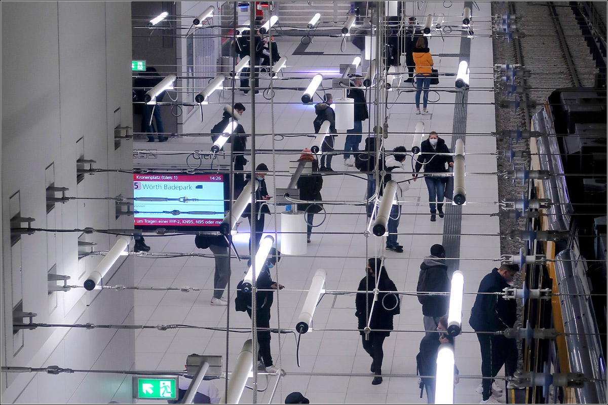 U-Haltestelle Kronenplatz - 

Das Lichtkonzept in den neuen Karlsruher U-Stationen stammt vom Designer Ingo Mauer. An quer durch den meist hohen Raum gespannten Seilen hängen die einzelnen Lichtröhren in unregelmäßiger Verteil und prägen so in einer weiteren Raumschicht die Haltestellen. Von den verglasten Zwischengeschossen fällt der Blick durch dies Netz hindurch auf die Bahnsteige. Hier die Haltestelle Kronenplatz.

12.01.2022 (M)

