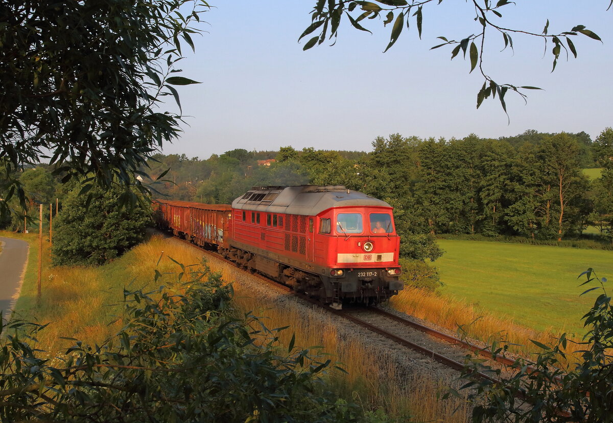 Übergabe von Zwickau nach Plauen-Zellwolle am 04.07.2023. Der Schrottzug mit der 232 117 am frühen Morgen bei Sonnenschein nahe Klärwerk Kürbitz.
