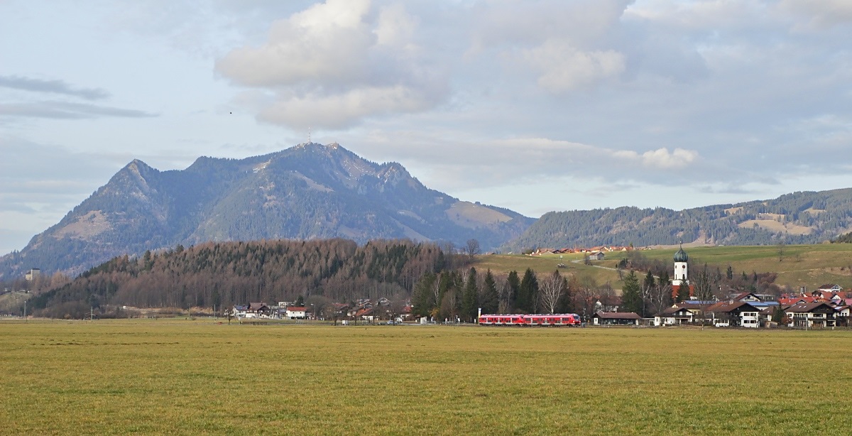Überragt vom 1.738 m hohen Grünten durchfährt ein 633-Doppel am 23.02.2023 Altstädten in Richtung Oberstdorf, das weiße Gebäude im Hintergrund ist das jetzt anderweitig genutzte Bahnhofsgebäude
