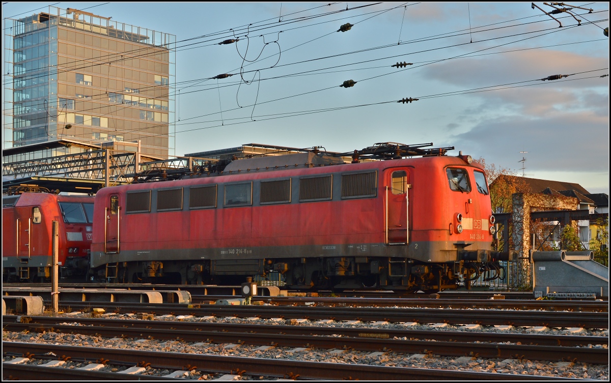 <U>Lichtspiele in Singen am Hohentwiel.</U> 

140 214-8 parkt auf der Brücke. Im Hintergrund der Hegautower, durch die eigenwillige Fassede selbst Hingucker. November 2013.