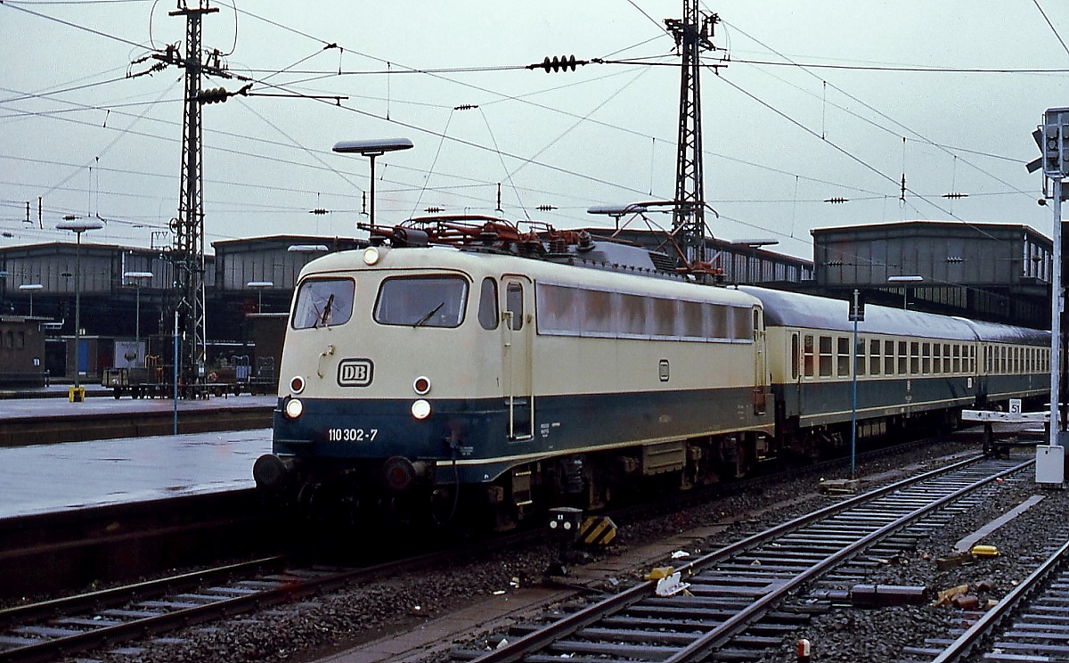 Um 1979 steht die 110 302-7 abfahrbereit vor einem Schnellzug im Düsseldorfer Hauptbahnhof. Noch stehen hier die alten Hallen, ein Jahr später wurde mit der Modernisierung bbegonnen.