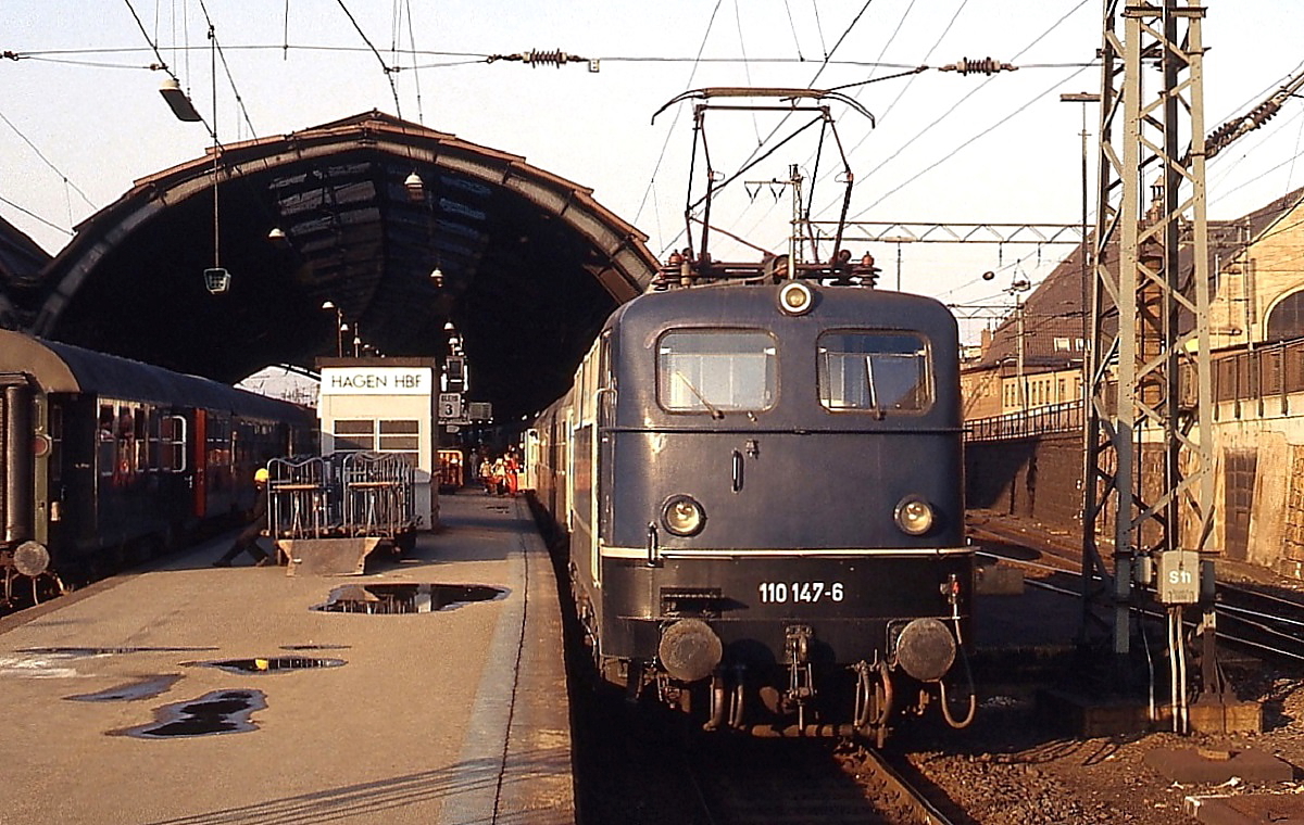 Um 1979 wartet 110 147-6 vor einem Nahverkehrszug Richtung Wuppertal im Hagener Hauptbahnhof auf Fahrgäste