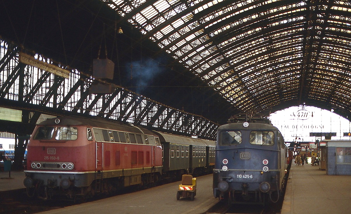 Um 1980 steht 110 425-6 vor einem D-Zug im Kölner Hauptbahnhof, daneben setzt sich 215 050-6 mit einem Nahverkehrszug in Richtung Gerolstein in Bewegung