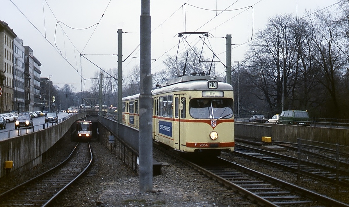 Um 1985 trifft der Achtachser 2854 aus Lörick kommend an der Haltestelle Opernhaus ein. Auf dem Nebengleis taucht ein Stadtbahnwagen der Linie 711 aus dem 1981 in Betrieb genommenen U-Bahn-Tunnel vom Kennedydamm auf. Mit der Inbetriebnahme des U-Bahnhofes Heinrich-Heine-Allee im August 1988 verkehren hier keine oberirdischen Bahnen mehr.