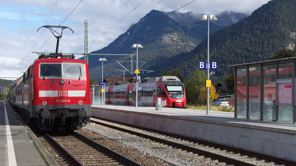 Umsteigen bitte! So heißt es seit April 2013. Seither dürfen die Lok bespannten Züge nicht mehr über die Grenze nach Österreich.
Als Grund ist zu lesen, dass die Türschließeinrichtungen der N-Wagen Schuld seinen, an anderer Stelle heißt es, dass es die Notbremsüberbrückung sei, die keine Zulassung für Österreich habe.

Dem Fahrgast mag dies egal sein, er muß nun halt den Zug in Mittenwald verlassen und in die Triebwagen der ÖBB Baureihe 4024 umsteigen.
An Gleis 1 steht 111 065-9 mit dem Zug nach München Hbf.
Bahnstrecke 5504 München Hbf. - Mittenwald Grenze am 07.10.2013