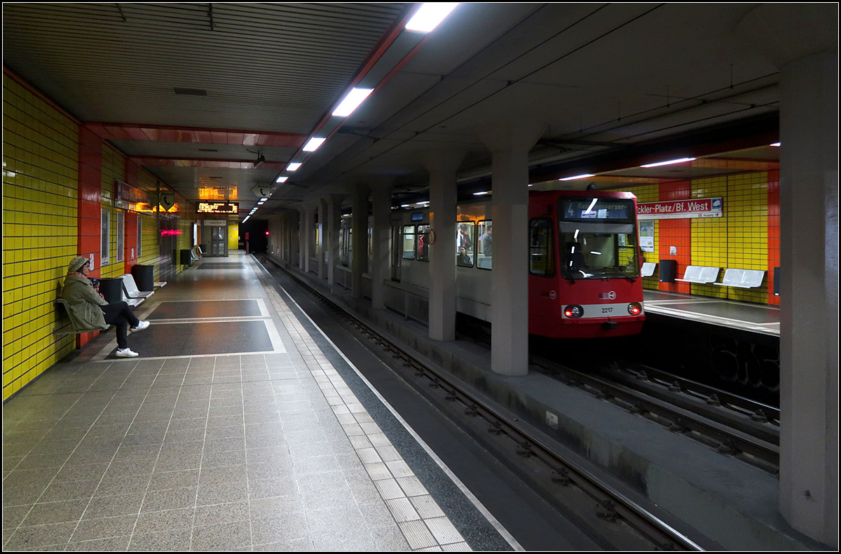 Unter der Venloer Straße -

Die Venloer Straße ist ein Hauptausfallstraße aus der Kölner Innenstadt in Richtung Nordwesten. Aufgrund der beengten Straßenbreite konnte kein eigener Bahnkörper in der viel befahrenen Straße angelegt werden und so dachte man hier schon früh daran, die Straßenbahn in die zweite Ebene, sprich in einen Tunnel zu verlegen. 

Das erste Teilstück ging 1985 in Betrieb und schließt an der ersten Tunnel (1968) der Kölner Straßenbahn an. Dieser führte von einer vorläufigen Rampe östlich des Friesenplatzes über den Appelhofplatz zur Haltestelle Dom/Hbf. Dort wurde zunächst an einem unterirdischen Dreieck gewendet.

Das erste Teilstück unter der Venloer Straße hat zwei unterirdische Station, einmal am Friesenplatz, wo seit 1987 auch die Ringstrecke unterirdisch kreuzt, und die Station Hans-Böckler-Platz/Bahnhof West (Bild). Erstmal in Köln wurde an beiden Bahnhöfen Hochbahnsteige angelegt, Teile des Bahnsteiges blieben aber für den Straßenbahnbetrieb weiterhin niedrig. Wegen dem Straßenbahnbetrieb wurde Seitenbahnsteige angelegt, die Gestaltung wirkt eher funktional.

Westlich der Station Hans-Böckler-Platz verzweigt sich die Strecke in Richtung Subbelrather Straße für die Linie 5. Bis zur Fertigstellung der Weiterführung unter der Venloer Straße wurden auch die Linien 3 und 4 über diesen Abzweig geführt mit einer vorübergehenden Umleitungstrecke im weiteren Verlauf der Subbelrahter Straße.

16.10.2019 (M)