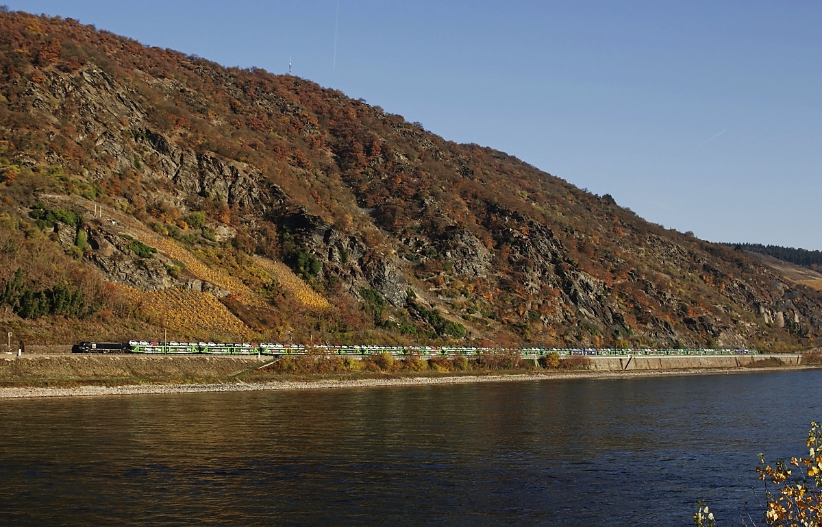 Unterhalb der Felsen des Rheinischen Schiefergebirges fährt eine MRCE-Vectron am 16.11.2018 mit einem Autozug nördlich von Kaub den Rhein entlang