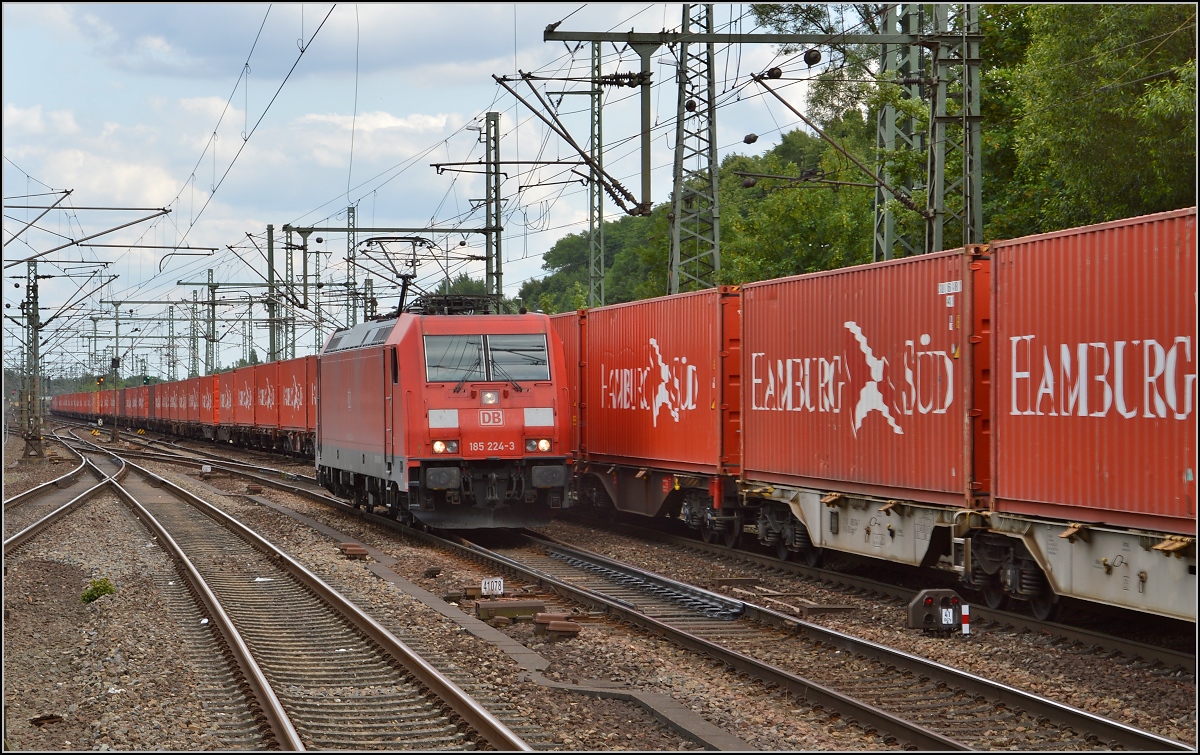 Unvermutet in Tarnfarbe. 185 224-3 vor rotem Containerzug. Hamburg Harburg, Juli 2015.