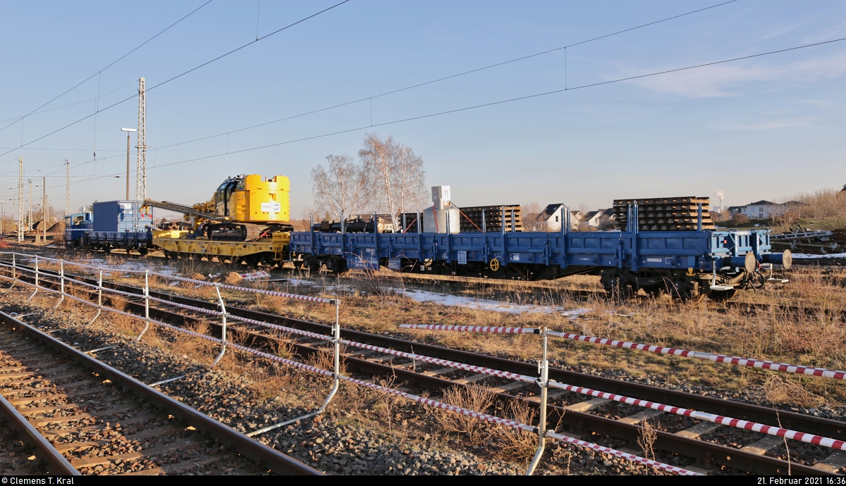 VDE 8 Komplexmaßnahme Halle Rosengarten–Angersdorf
▶ Standort: Bahnhof Angersdorf

Während der Baubetrieb wahrscheinlich wegen der frostigen Verhältnisse an den Tagen zuvor ruht, steht der seit Januar hier stationierte Bauzug - wenn auch nicht vollständig - in der alten Abstellgruppe. Eingereiht sind zwei vierachsige Flachwagen der Gattung  Res  mit einem Container und weiterem Baumaterial sowie ein sechsachsiger Flachwagen der Gattung  Samms 710  mit einer Ramme Delmag G42. Ganz vorn hängt 335 014-7  Elli  (333 014-9 | Köf III).
Aufgenommen von Bahnsteig 2/3.

🧰 Jaeger Spezial- und Tiefbau GmbH + Co KG (Jaeger Bernburg)
🚩 Bahnstrecke Halle–Hann. Münden (KBS 590)
🕓 21.2.2021 | 16:36 Uhr