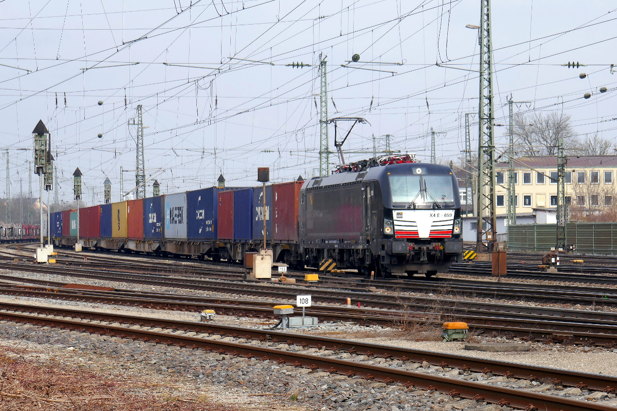 Vectron 193 659 der MRCE beschleunigt einen langen Güterzug aus dem Bahnhof Treuchtlingen in Richtung Augsburg. Das Gebäude rechts im Hintergrund gehört (oder gehörte) der Post und hatte früher sogar einen Gleisanschluß. Freitag, 18. März 2022 