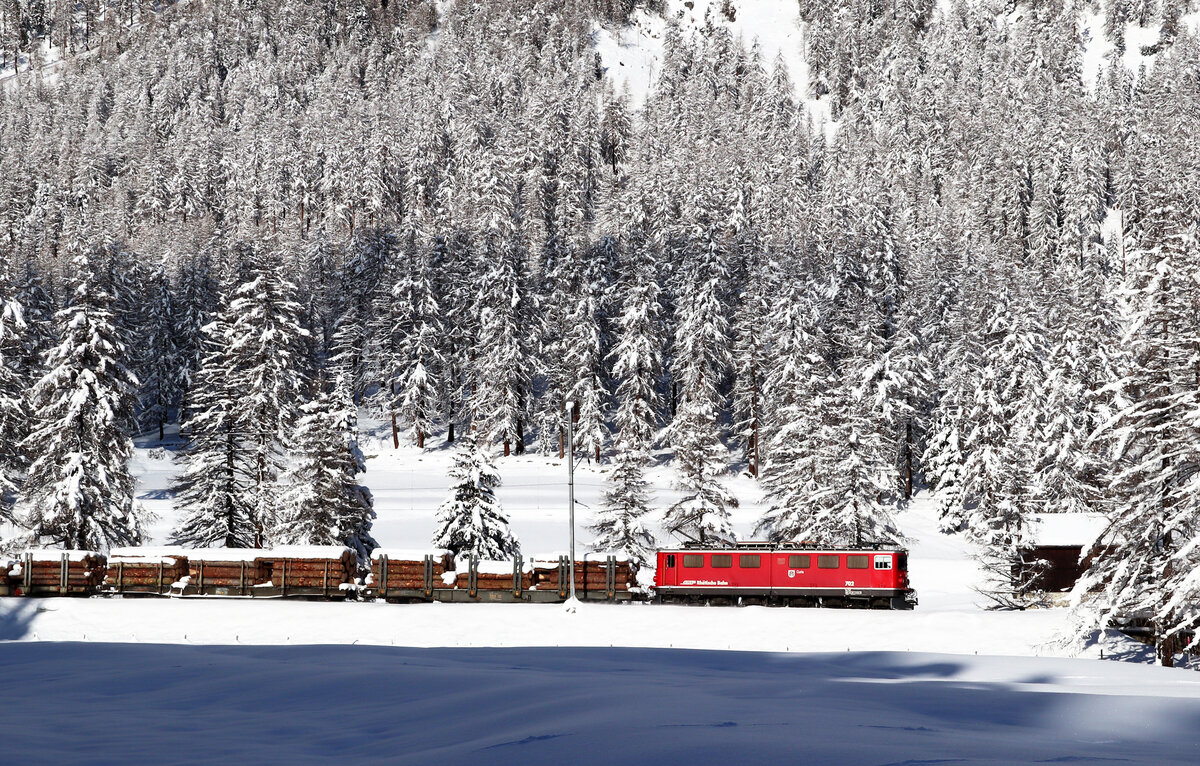 Verschneite Holzwagen in verschneiter Landschaft: Ge 6/6 702 zieht einen Güterzug durch das Val Bever zwischen Spinas und Bever. Bever, 10.12.2020