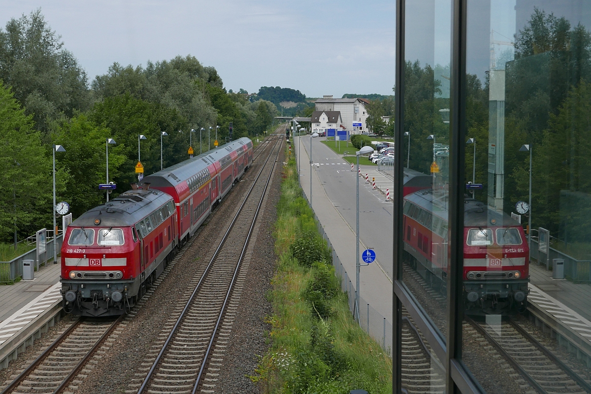 Versuch, den sich auf der Verglasung des Aufzuges der Fugngerberfhrung spiegelnden Zug zusammen mit dem direkt zu fotografierenden Zug in einem Bild festzuhalten. 218 427-3 durchfhrt mit den Wagen des IRE 4215 von Stuttgart nach Lindau die Haltestelle Biberach Sd (31.07.2017).