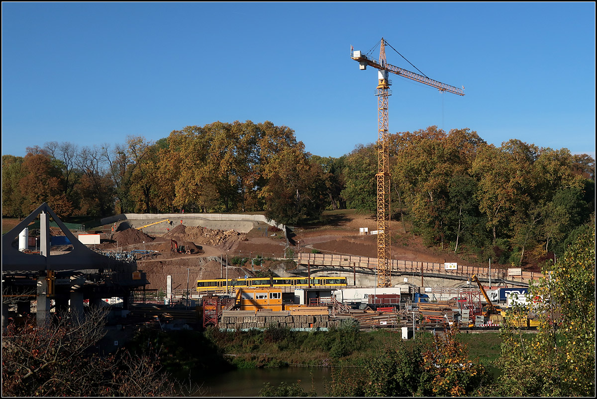 Verwundeter Talhang -

Ein Zug der U14 fährt durch die offenen Wunden am Hang des Rosensteinparkes. Über und unter der Stadtbahntrasse entstehen hier Tunnelportale für den Schienen und Straßenverkehr. Links über der Stadtbahn haben die Arbeiten an den beiden Tunnelportalen begonnen, einmal für die zweigleisige Röhre des Fern- und Regionalverkehrs zum anderen für den S-Bahntunnel der auf anderer Trasse über die neue Station Mittnachtstraße zum Stuttgarter Hauptbahnhof führen wird. Die Stadtbahn befährt hier ein provisorisches eingleisiges Brückenbauwerk über die Baugrube des Straßentunnels. Die beiden zweispurigen Tunnelröhren für die Bundesstraße 10 unter dem Park sind schon aufgefahren.

Links im Bild ist ein Teil der neuen Neckarbahnbrücke erkennbar. 

12.12.2018 (M)