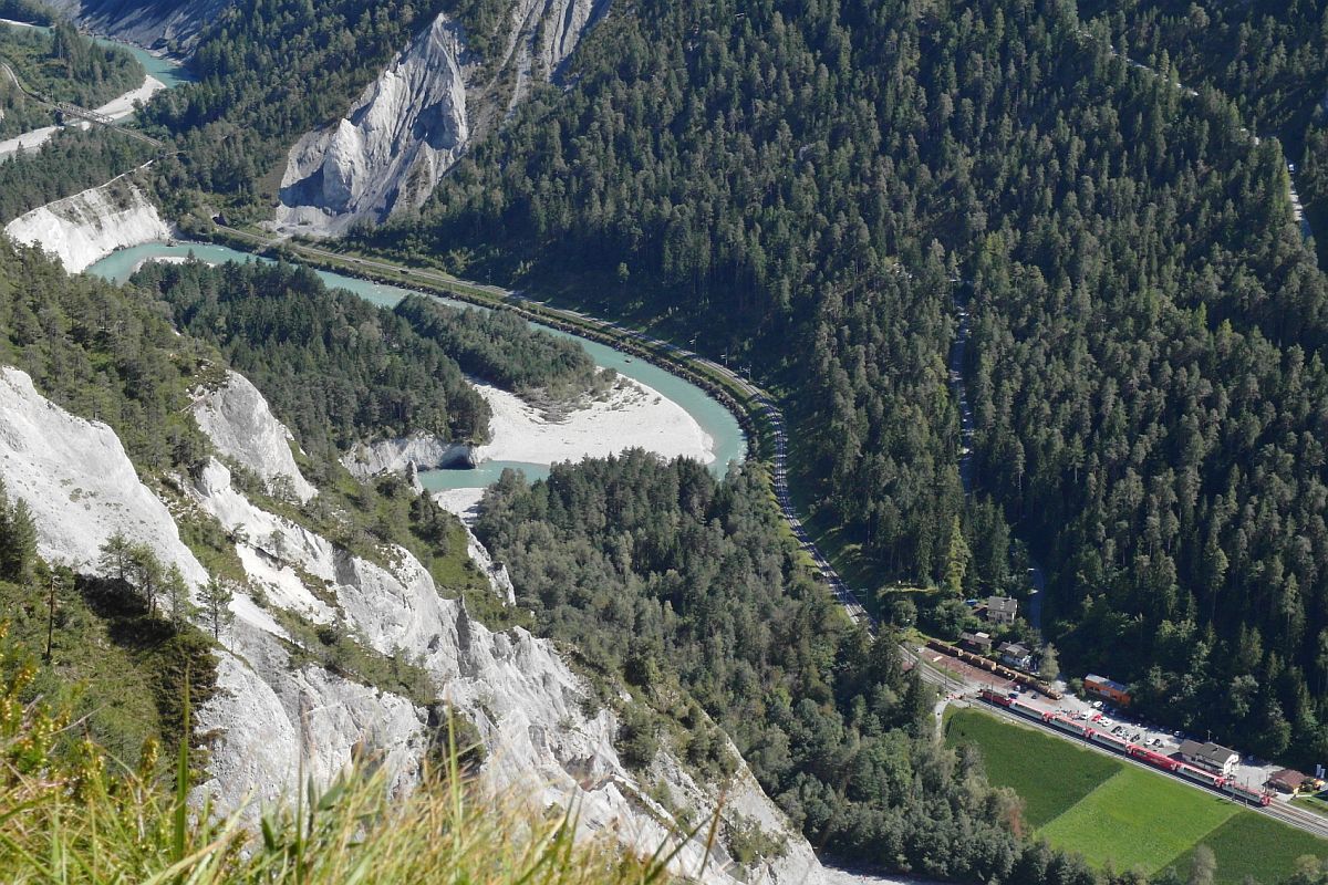 Viel Landschaft, wenig Bahn. Kaum zu erkennen sind die Wagen des Glacier-Express, GEX 904, Zermatt - St. Moritz in der Station Versam-Safien (24.08.2014).