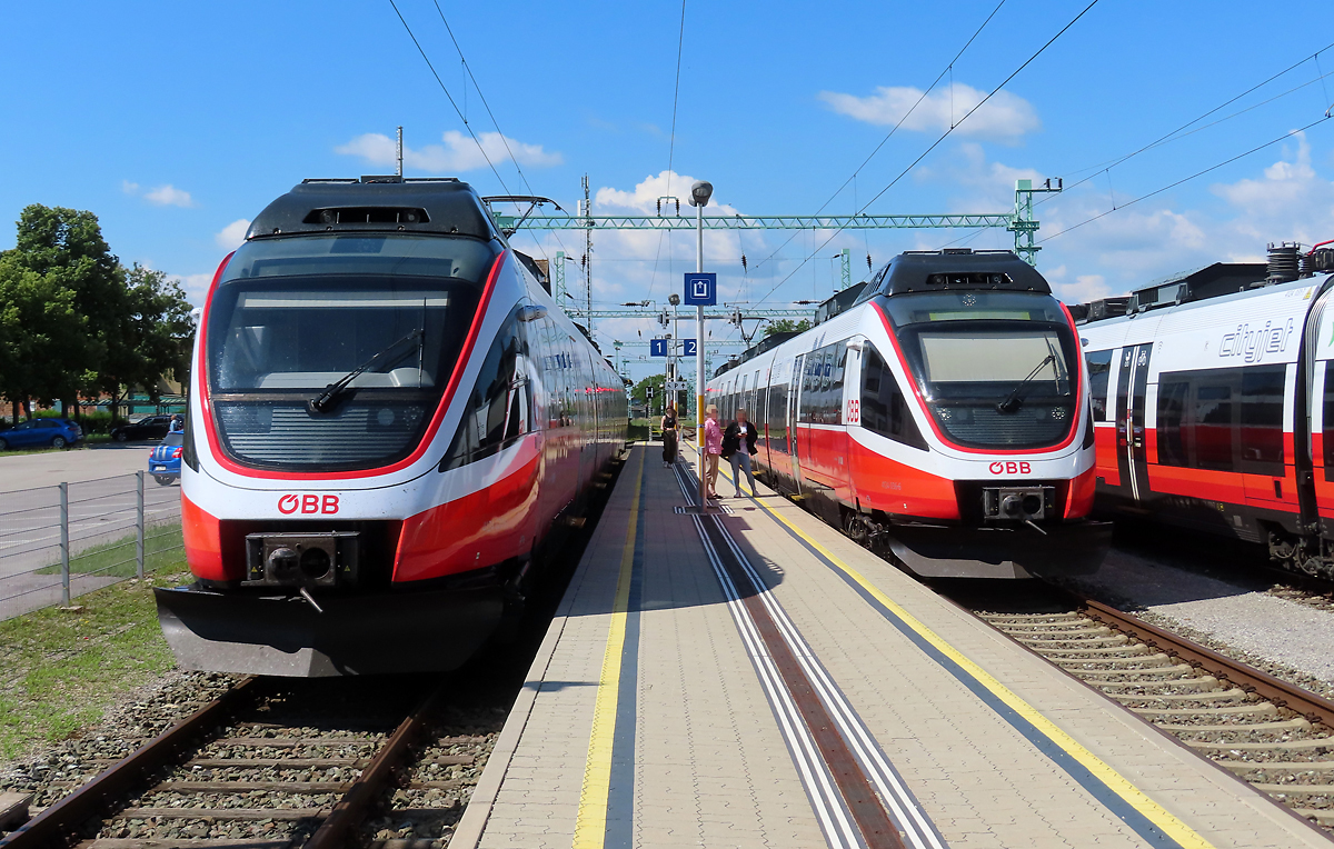 Viele Talente in Pamhagen: links und rechts mehrere Talent-Triebzüge im Stilllager, in der Mitte wartet der Regional-Express nach Neusiedl am See auf seine Abfahrt. Pamhagen, 17.6.2023