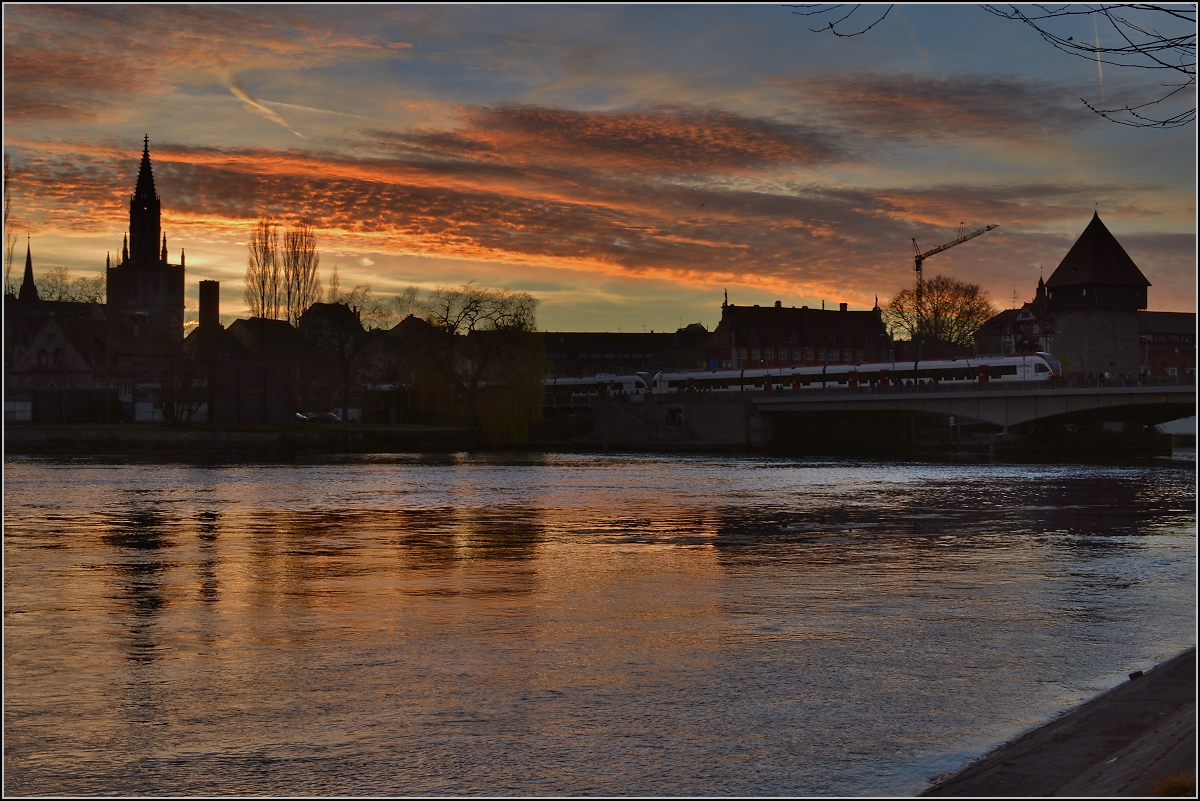 Vielfarbig leuchtet der Himmel und lässt seine farbigen Spuren auch im Dunklen walten, nur schwach schimmert der Seehas auf der Rheinbrücke. Konstanz, Dezember 2015.
