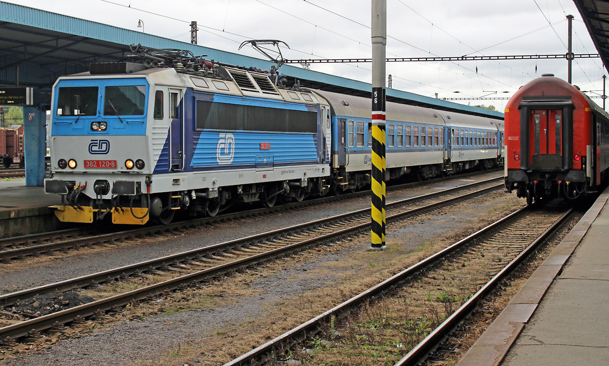 Vom nordwestböhmischen Cheb gibt es 2 Schnellzuglinien nach Prag. Die 362 120 hat am 04.10.2016 die Aufgabe, den R611 (Karlex) zu befördern und fährt am Südrand des Erzegebirges über Karlovy Vary und Chomutov bis Usti nad Labem, dort wird wegen des Richtungswechsels auch die Lok getauscht. Der rechte Zug, der nur die Rücklichter zeigt, ist der Rx761 (Visehrad), der wird, obwohl etwas später abfahrend, 47 Minuten eher in der tschechischen Hauptstadt ankommen, die Strecke über Stribro und Plzen ist halt etwas kürzer. Die Zweisystem-Unterstützung der 362er ist bei beiden Zügen notwendig, da unterwegs vom 25kV/50Hz-Netz in Westböhmen auf das 3kV-Gleichstromnetz um Prag herum umgeschaltet werden muss.