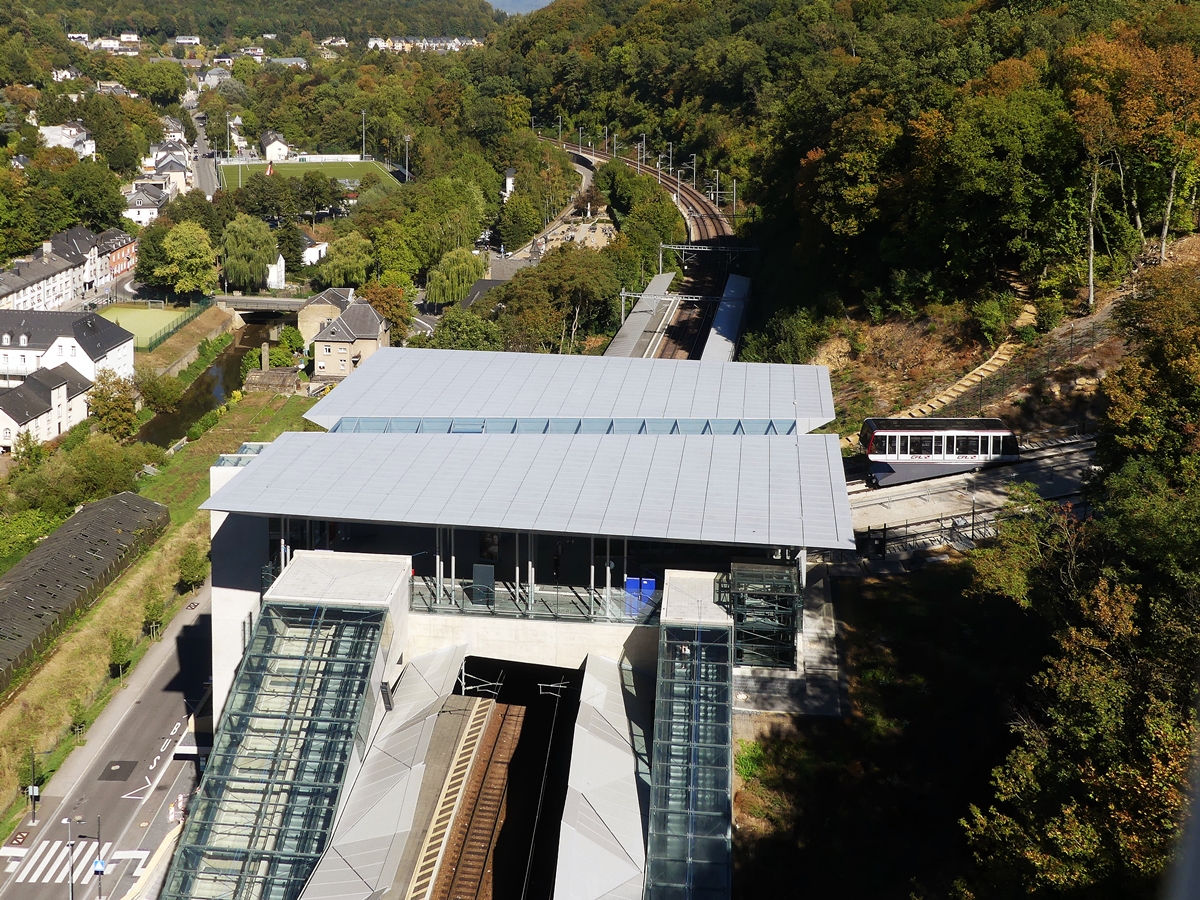 Vom Pont Grande-Duchesse Charlotte (Rout Brck) in der Stadt Luxemburg kann man den darunter liegenden CFL Bahnhof Pfaffenthal-Kirchberg, sowie die namensgleiche CFL Standseilbahn fotografieren. 27.09.2018 (Jeanny)

Durch den 2017 in Betrieb genommenen Bahnhof Pfaffenthal-Kirchberg wurde Luxemburgs Topografie radikal verndert. Die Standseilbahn schafft eine Anbindung der Intercity- und Regionalzge an den ffentlichen Nahverkehr auf dem Kirchberg-Plateau, einem der Gebiete mit der hchsten Arbeitsplatzdichte im Groherzogtum. ber Aufzge werden der Talboden und ein Teil der Unterstadt erschlossen. Als neuer Vernetzungspunkt der ffentlichen Verkehrsnetze trgt sie zur Entlastung des Hauptbahnhofs bei und verkrzt auf bestimmten Strecken die Reisezeit um mehr als 20 Minuten.

Der neue Bahnhof ist das Ergebnis eines entschiedenen politischen Willens, den motorisierten Individualverkehr zu begrenzen und eine nachhaltige Mobilitt zu frdern: Zug, Tram, Langsamverkehr.
