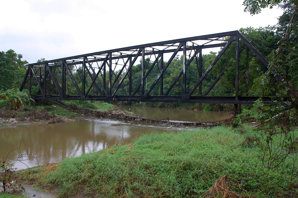 Von der 1978 eingestellten Bahnlinie Hat Yai Junction - Songkhla sind noch einige Relikte vorhanden. Ungefähr beim Strecken-Km 938 führt eine 60m lange Fachwerkbrücke über den Khlong Nam Noi. Der angebaute Fußgängersteg ist in der Zwischenzeit abgerosted und in den Fluss gestürzt. Bild vom 07.Jänner 2023 bei regnerischem Wetter.