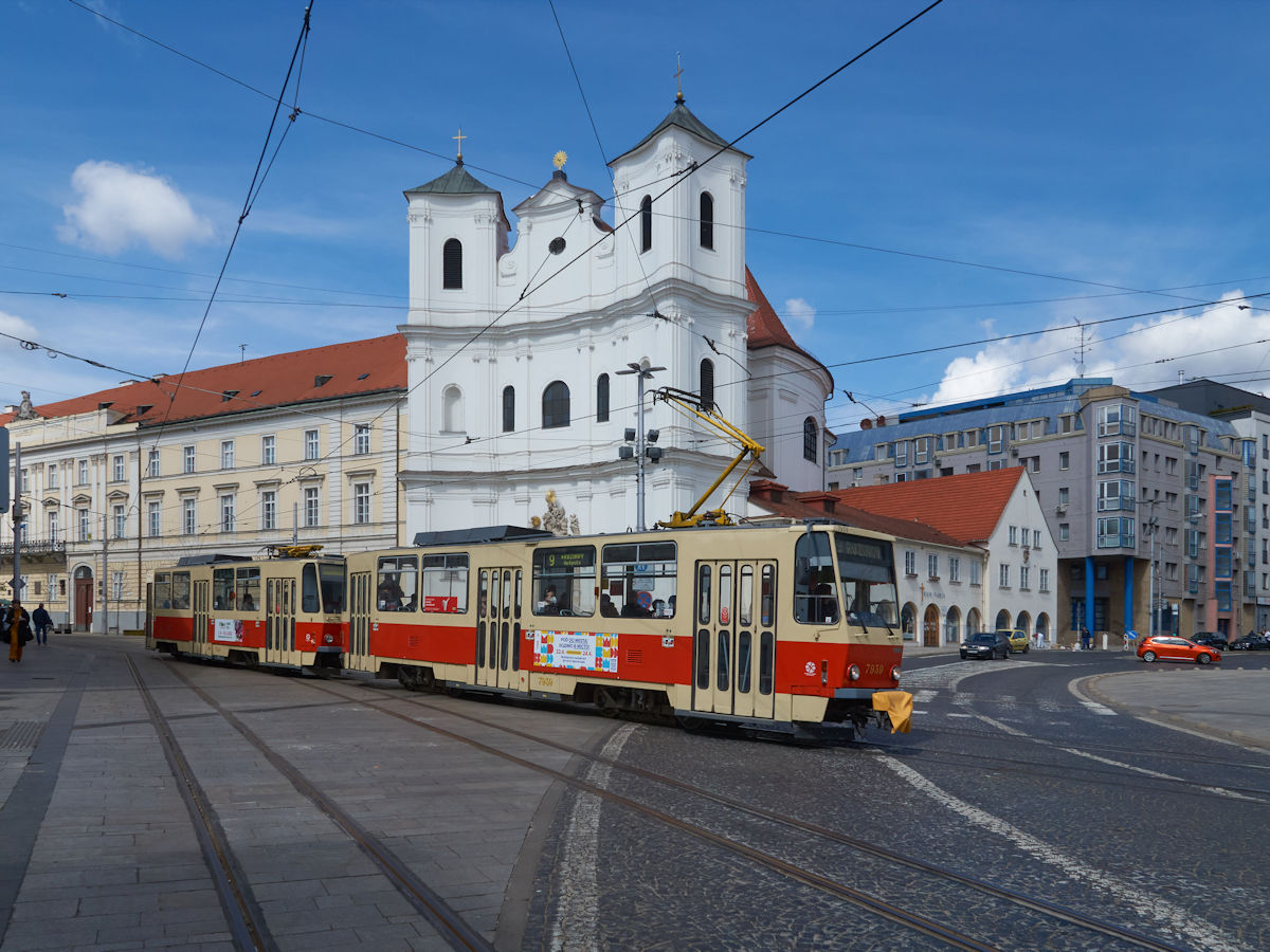Von Karlsdorf (Karlova Ves) kommend überqueren die T6A5 7939 und 7940 der Straßenbahn Bratislava den Hurbanplatz auf dem Weg nach Rosenheim (Ružinov). Hier befindet sich die barocke Trinitarierkirche und das Dreifaltigkeitskloster.